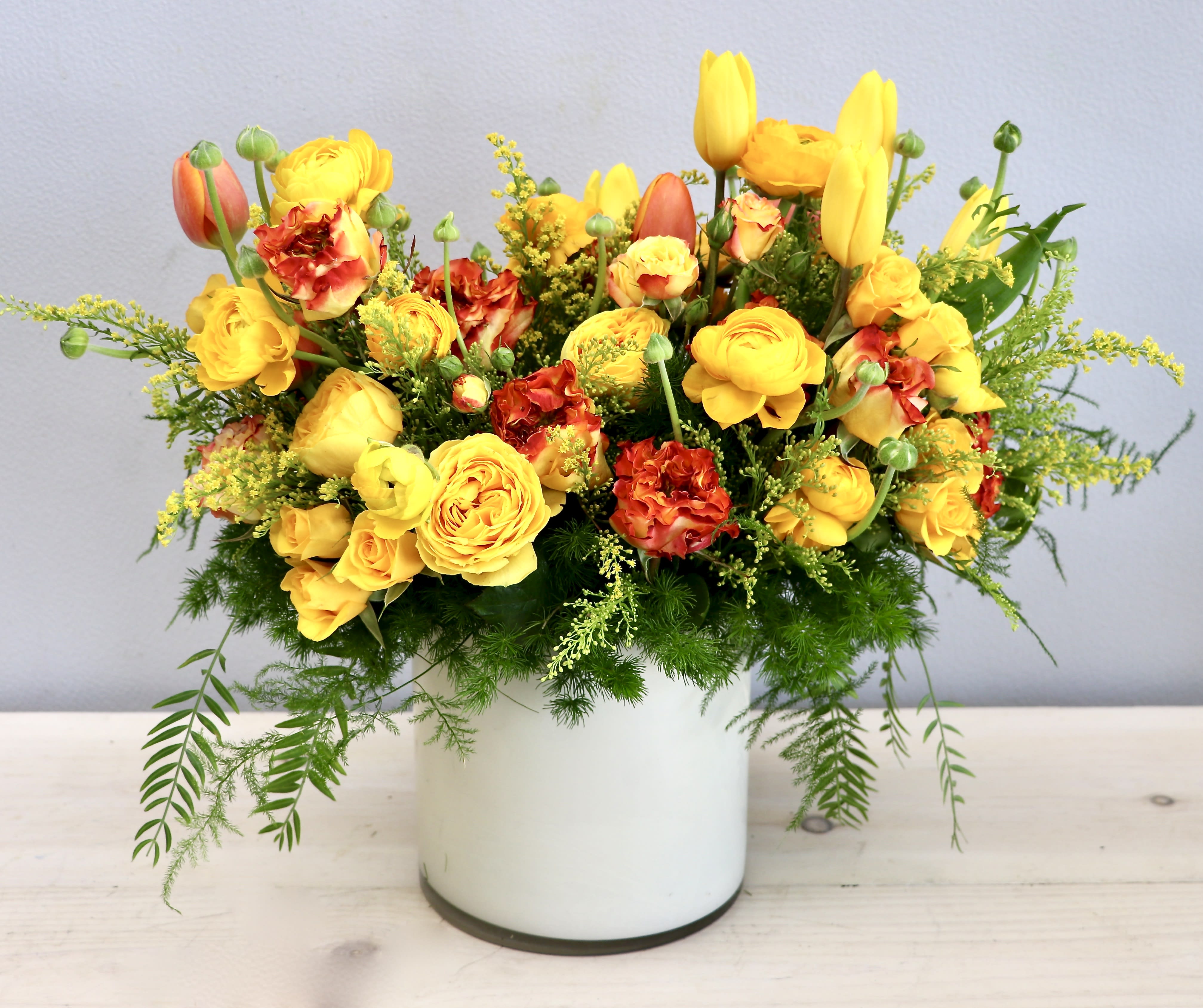 Bright yellow and orange mixed flower arrangement in a white cylinder vase