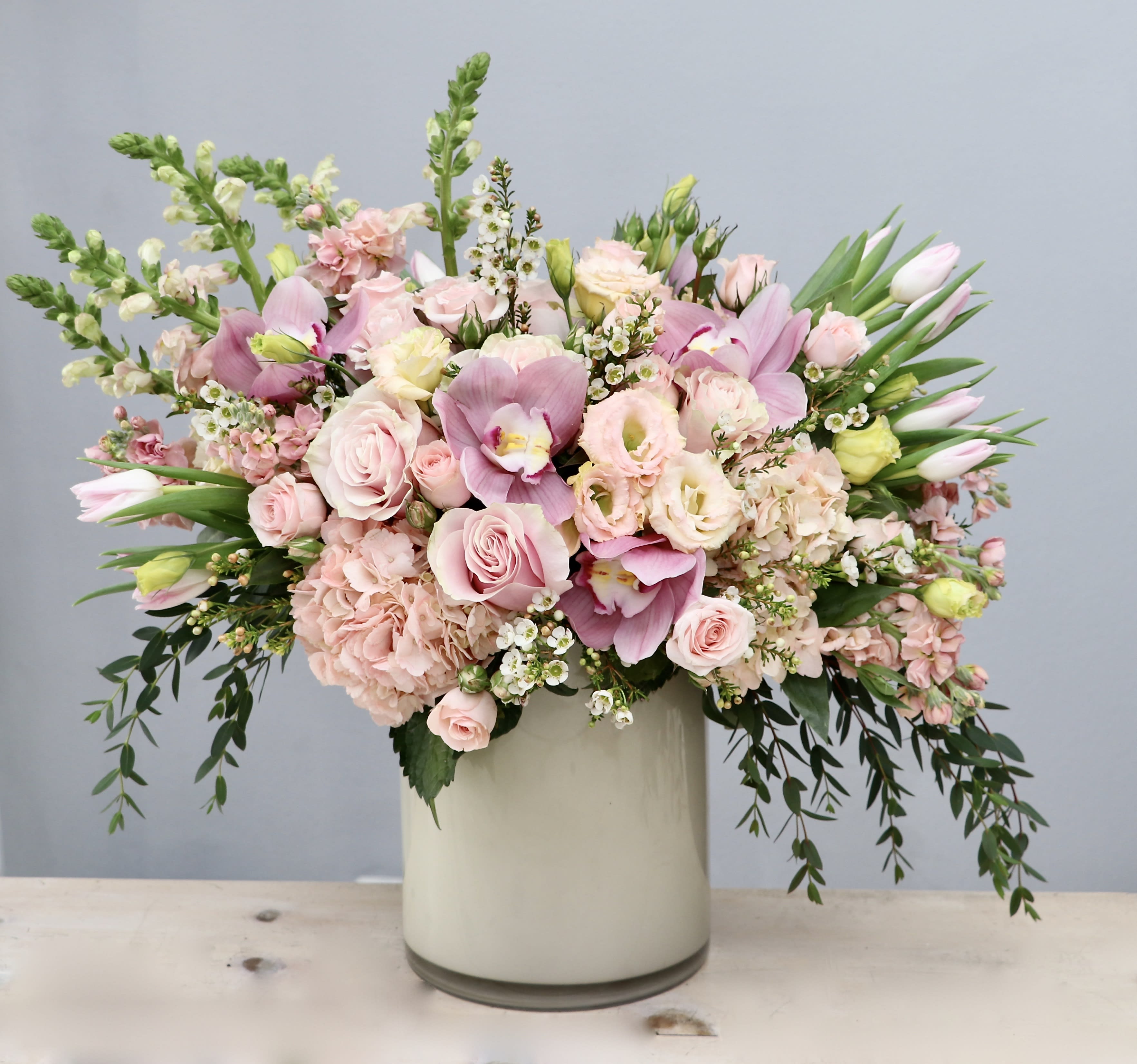 Large pastel pink and white flower arrangement with roses, orchids, and tulips in a white cylinder vase