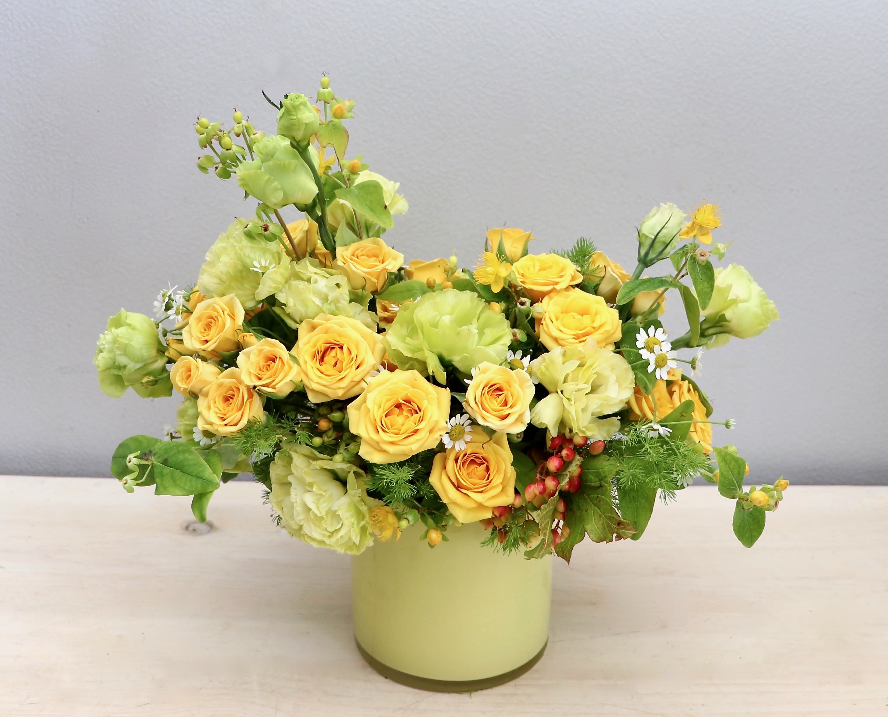 Yellow roses and pale green carnations arranged in a light green cylinder vase