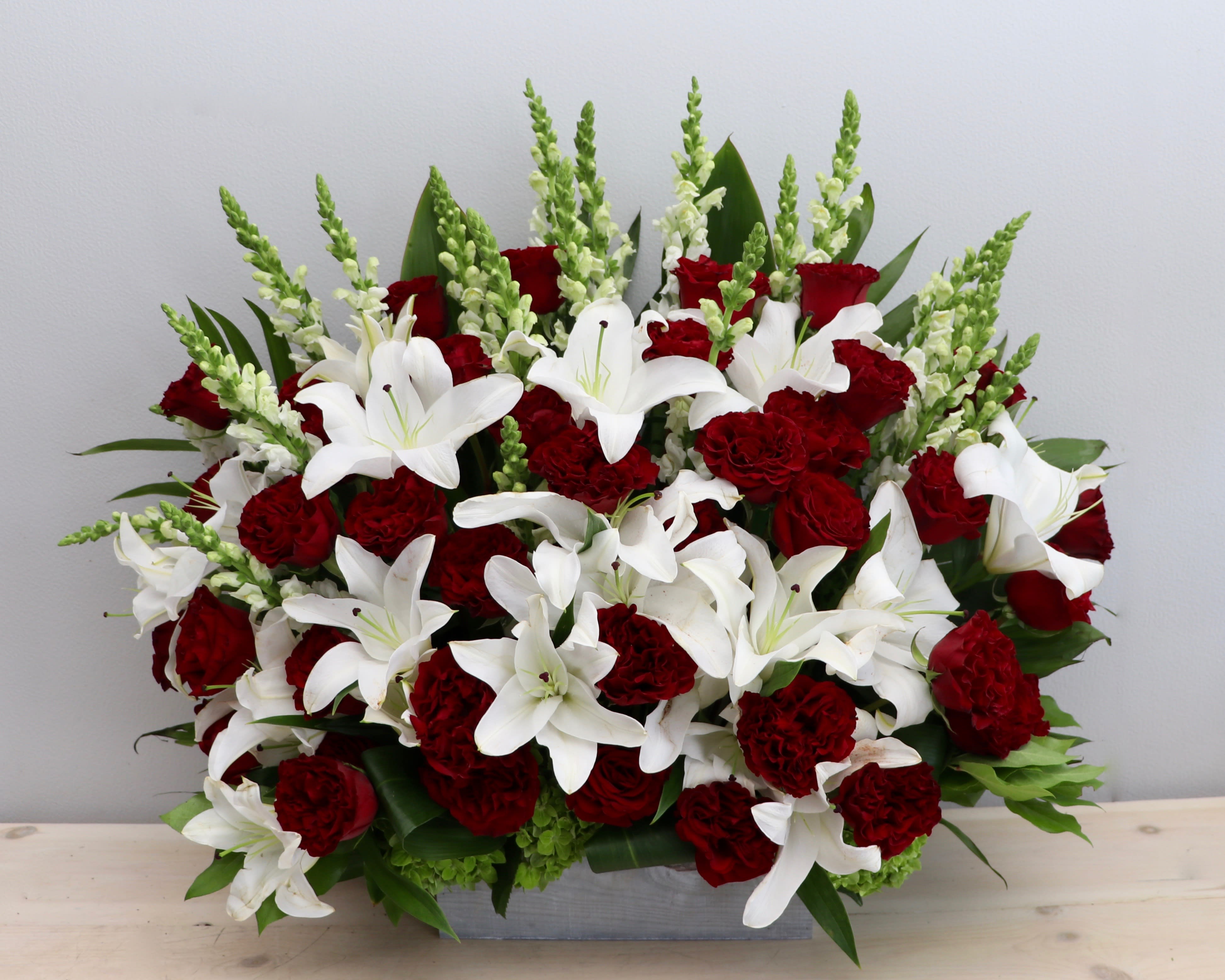 Red roses and carnations with white lilies and snapdragons in a low rectangular container