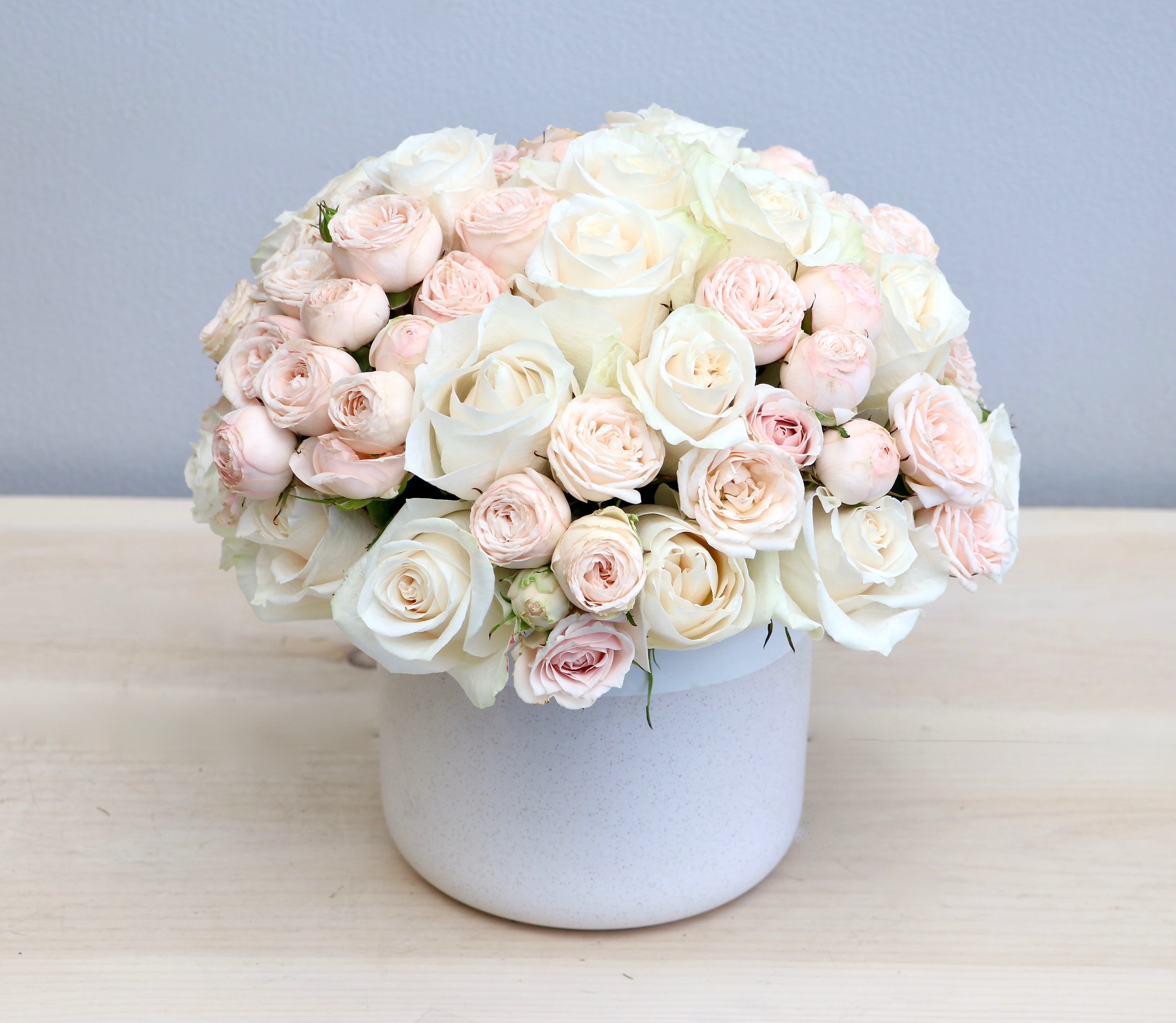 Dome-shaped arrangement of white and blush roses in a white ceramic pot
