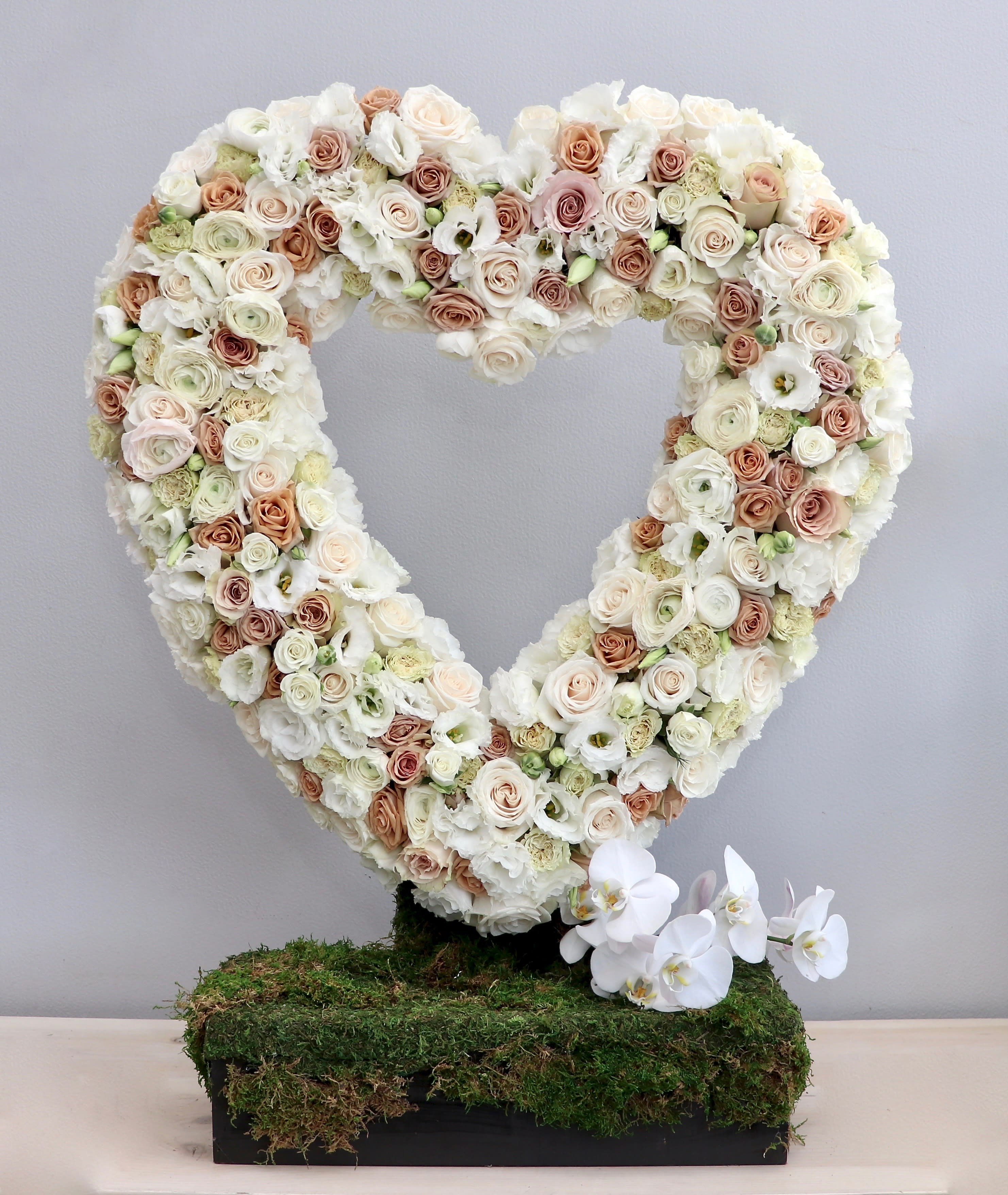 Heart-shaped standing wreath of ivory and blush roses on a moss-covered base with white orchids at the bottom