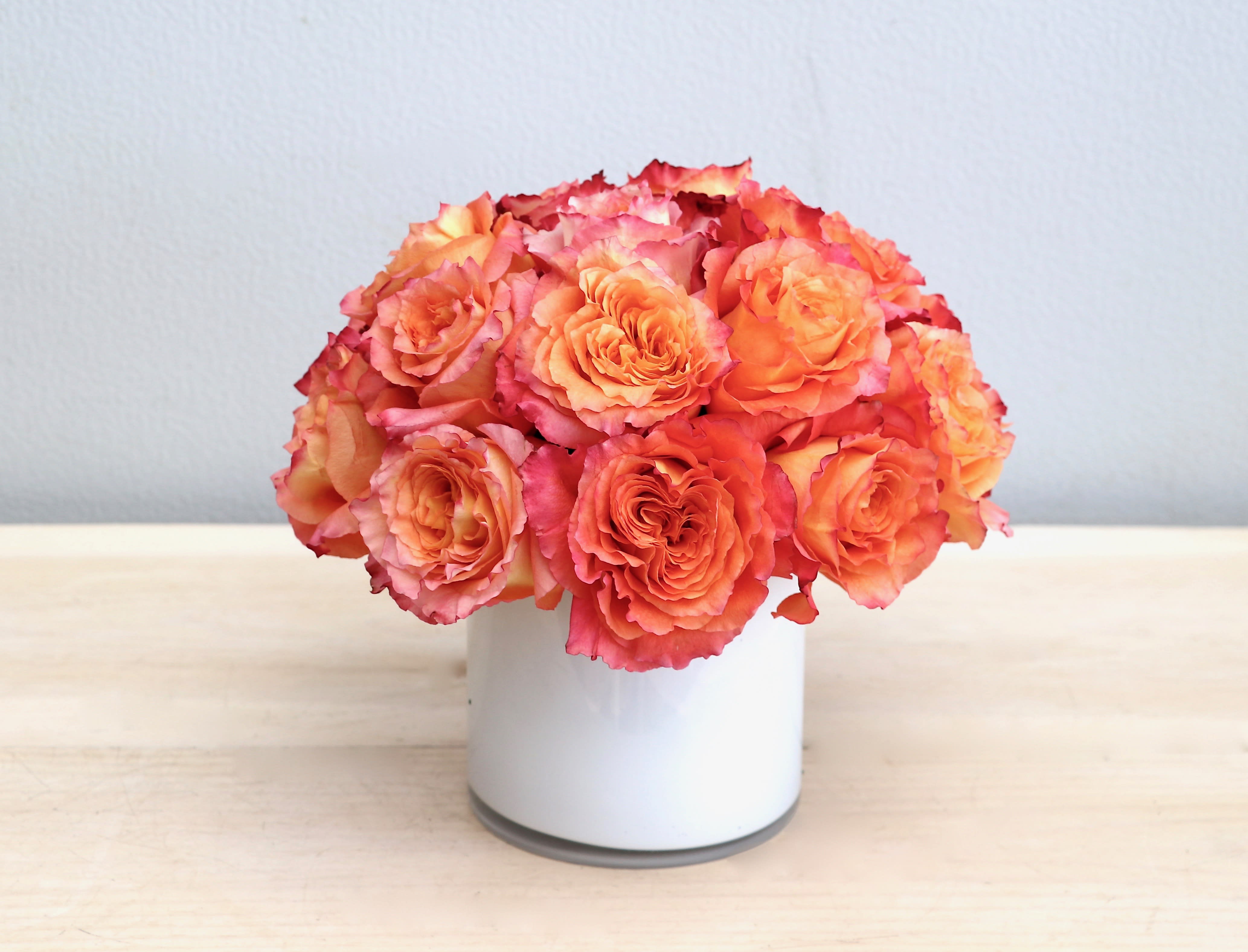 Compact arrangement of orange and pink roses in a white cylinder vase