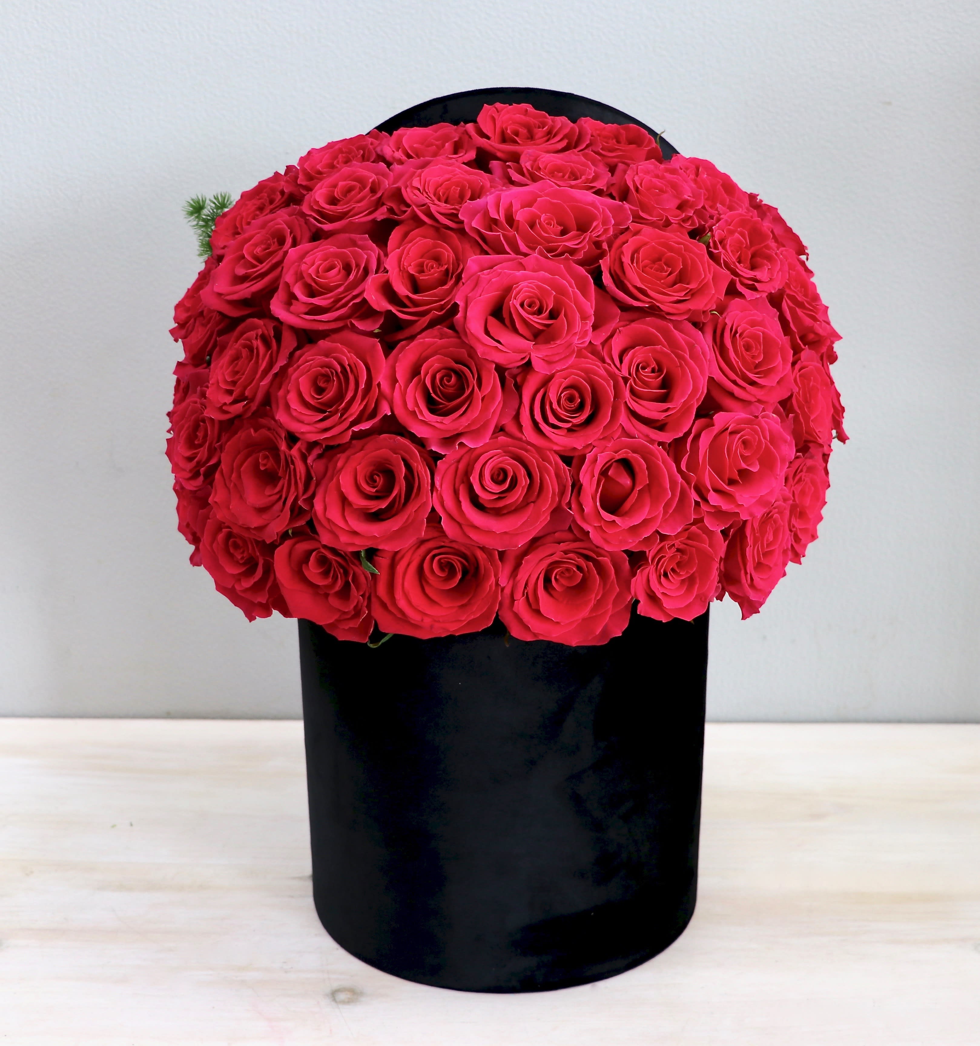 Tight dome of bright pink roses arranged in a tall black cylindrical box.