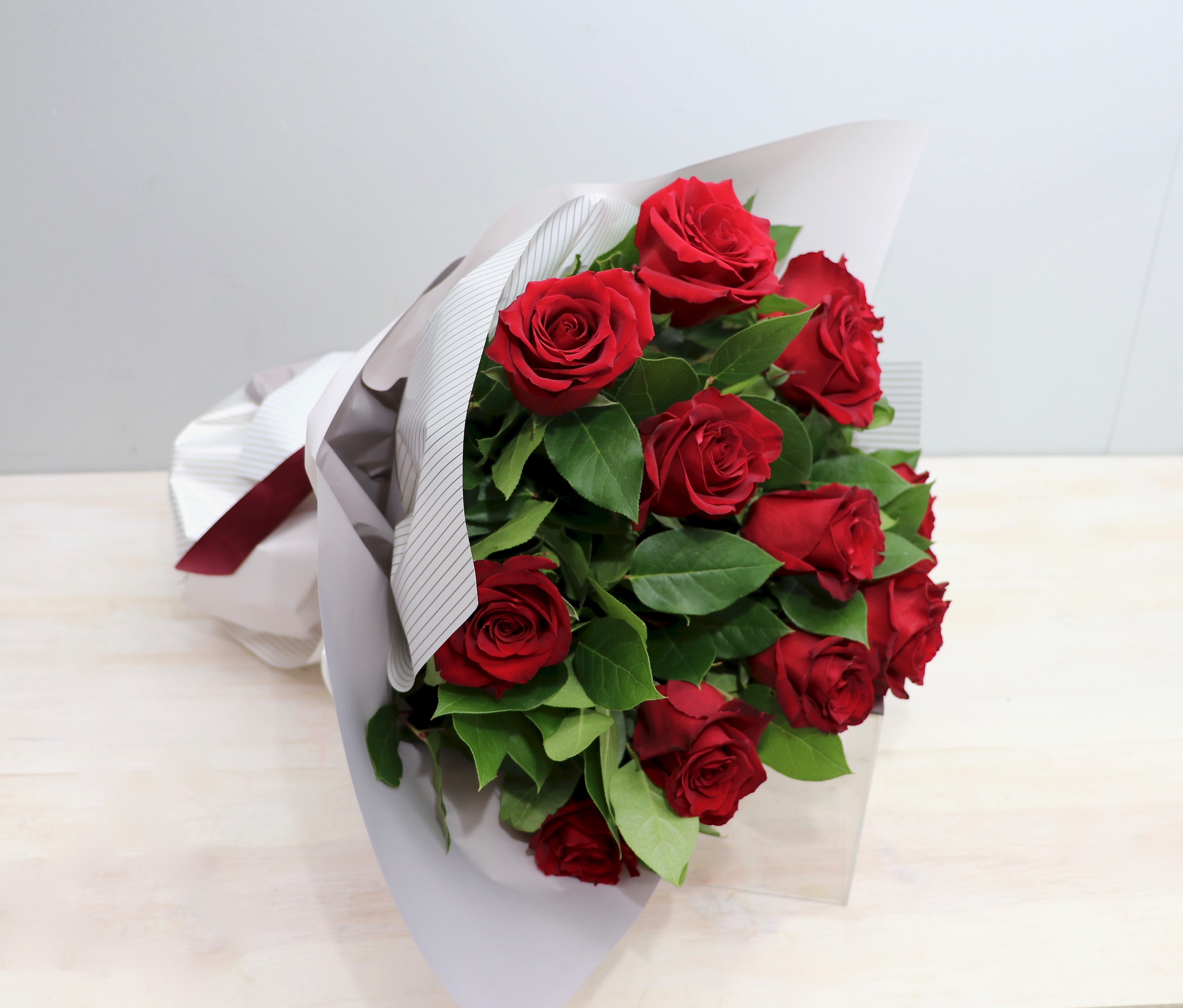 Hand-tied bouquet of red roses wrapped in white paper with a red ribbon