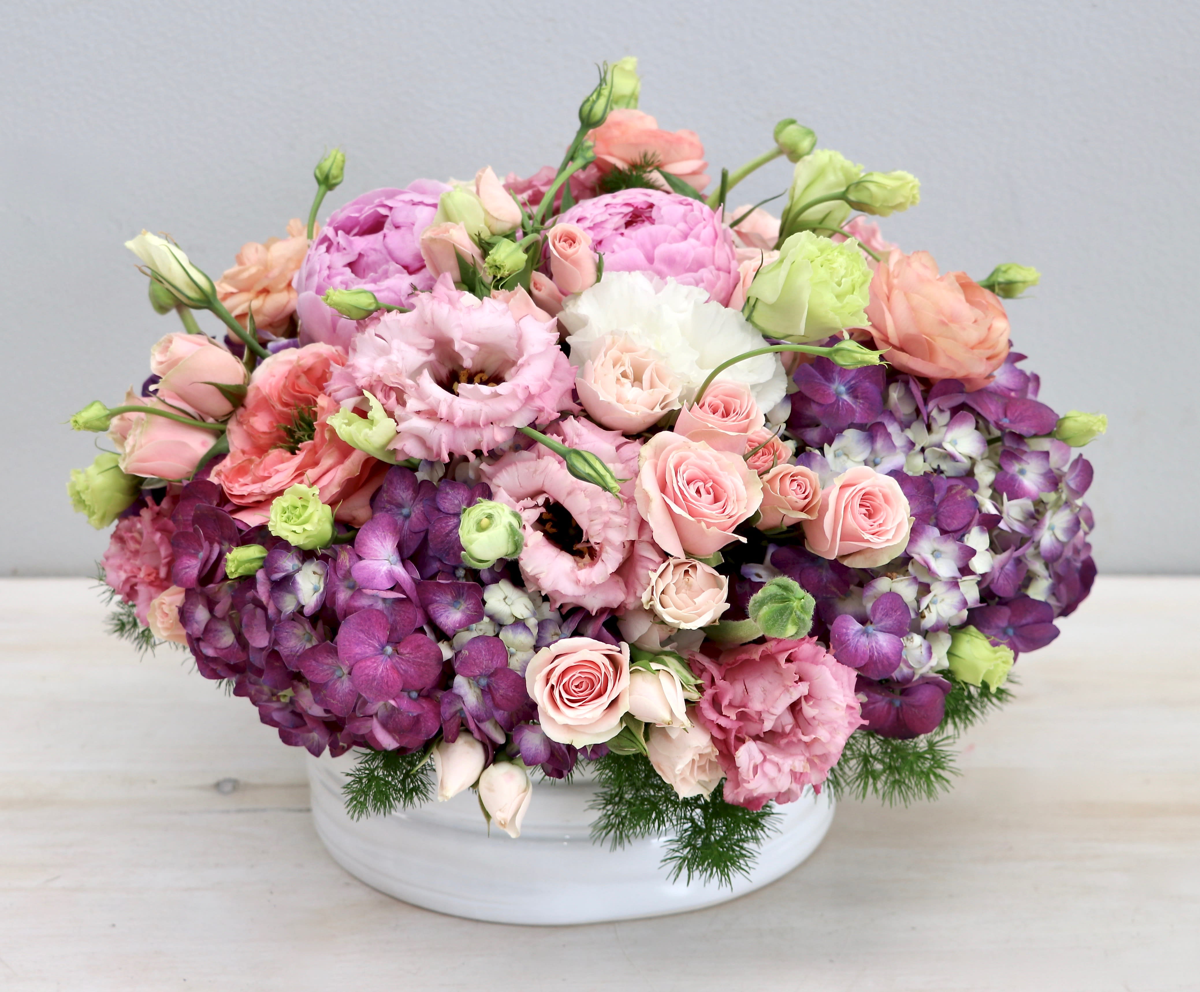 Low arrangement of pink and purple flowers in a white ceramic bowl