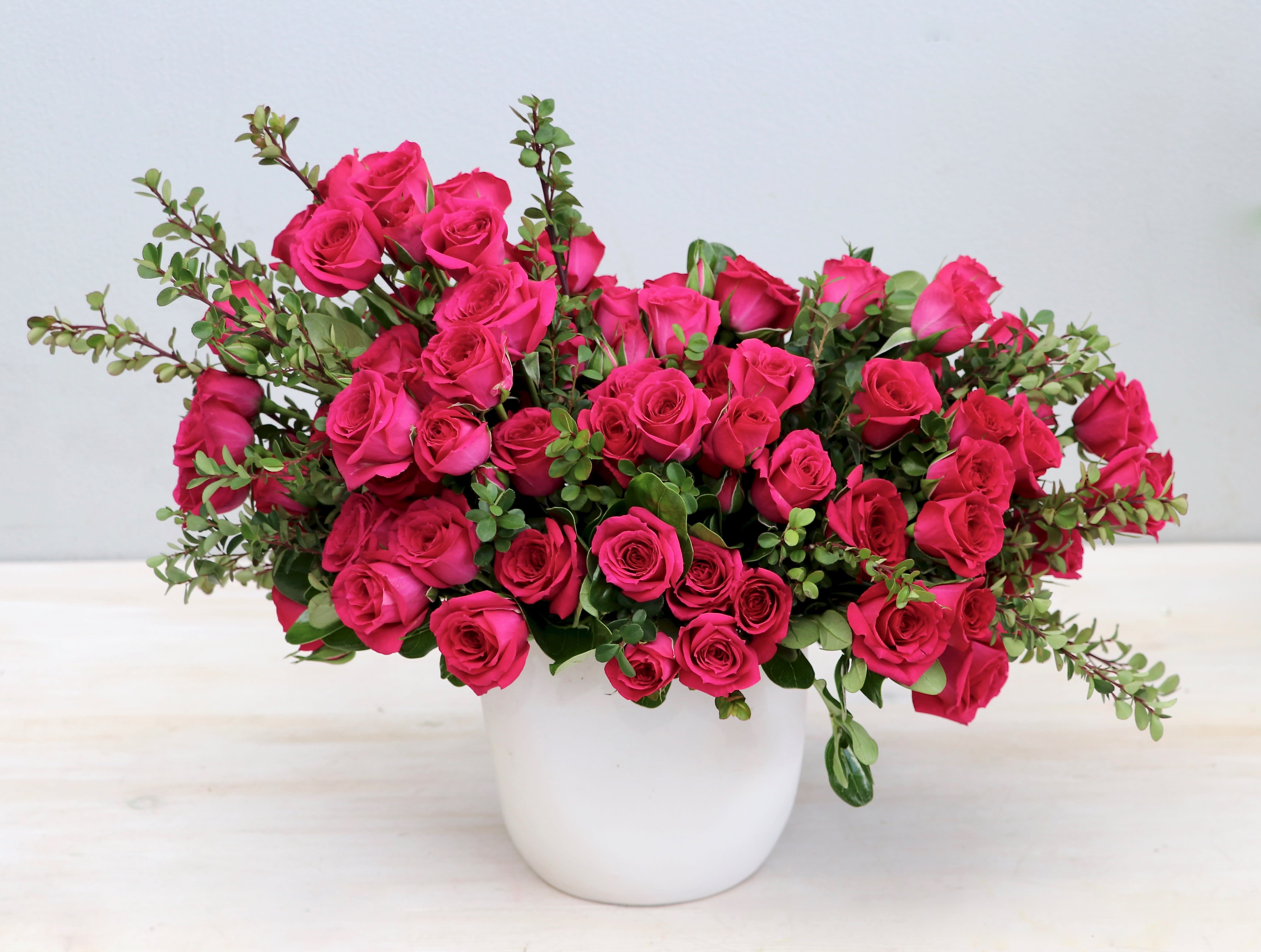 Lush arrangement of hot pink roses with green accents in a white ceramic pot
