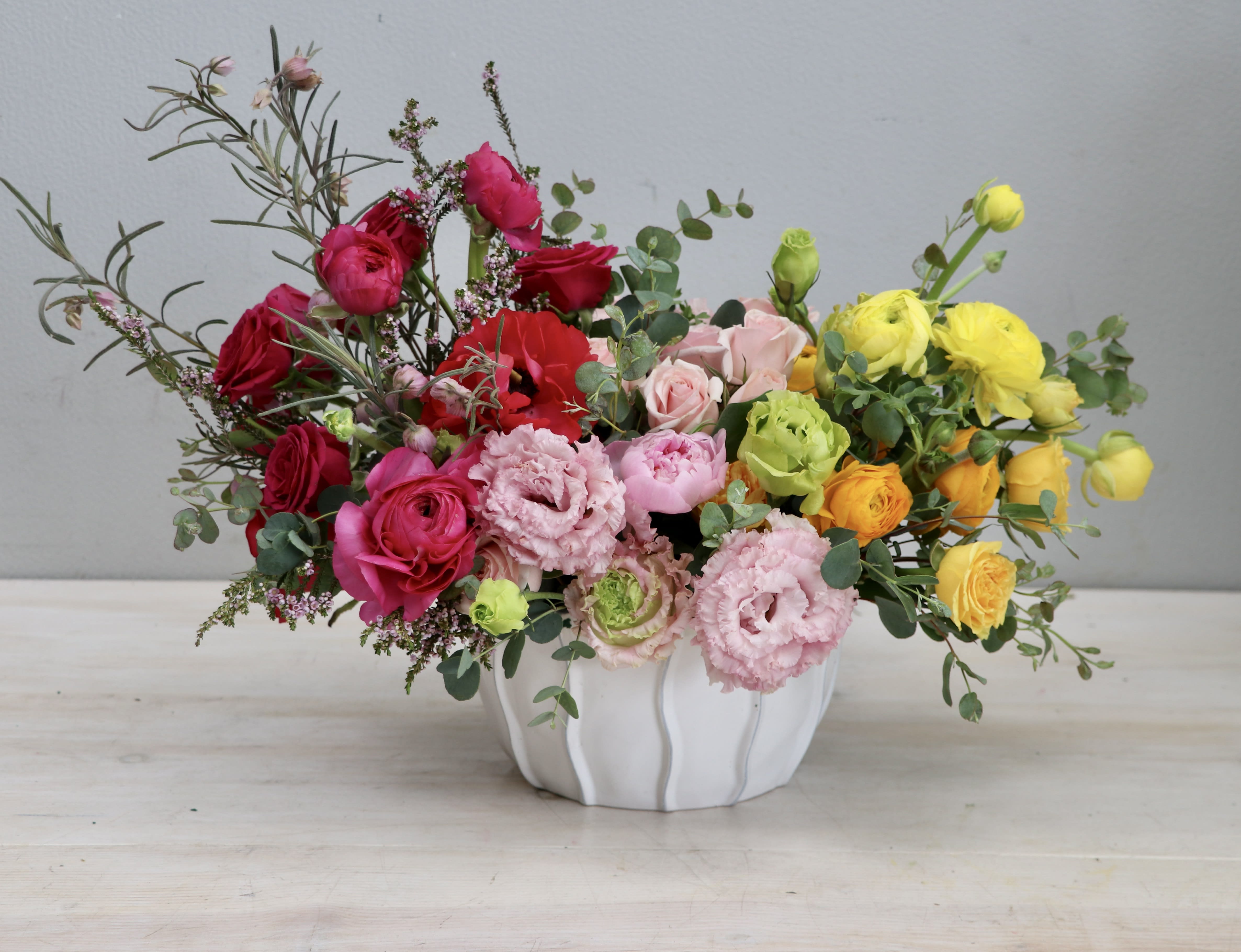 Low centerpiece of red, pink, yellow, and orange flowers in a white ceramic bowl.