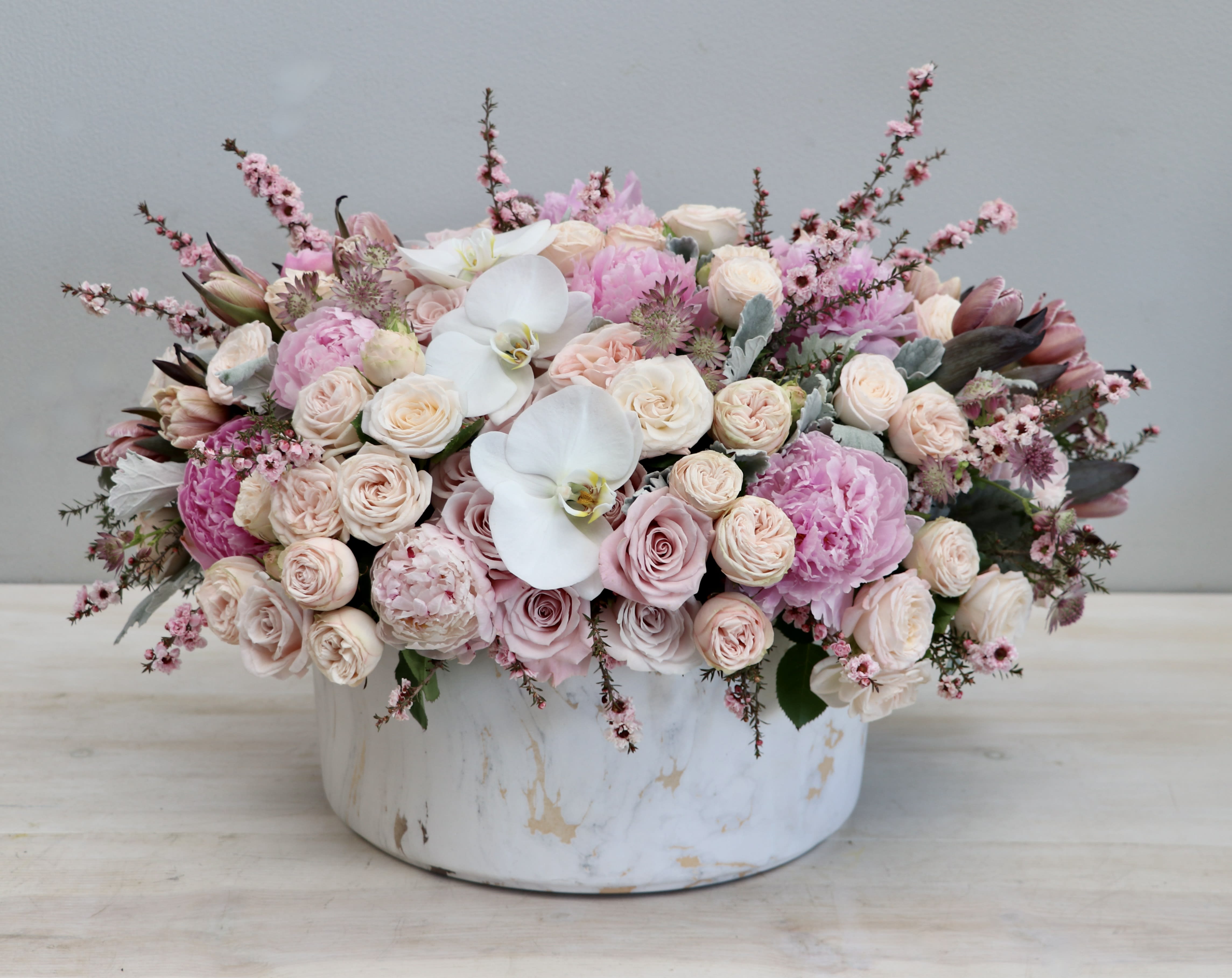Low pink and white arrangement of roses, peonies, and orchids in a round white ceramic vase