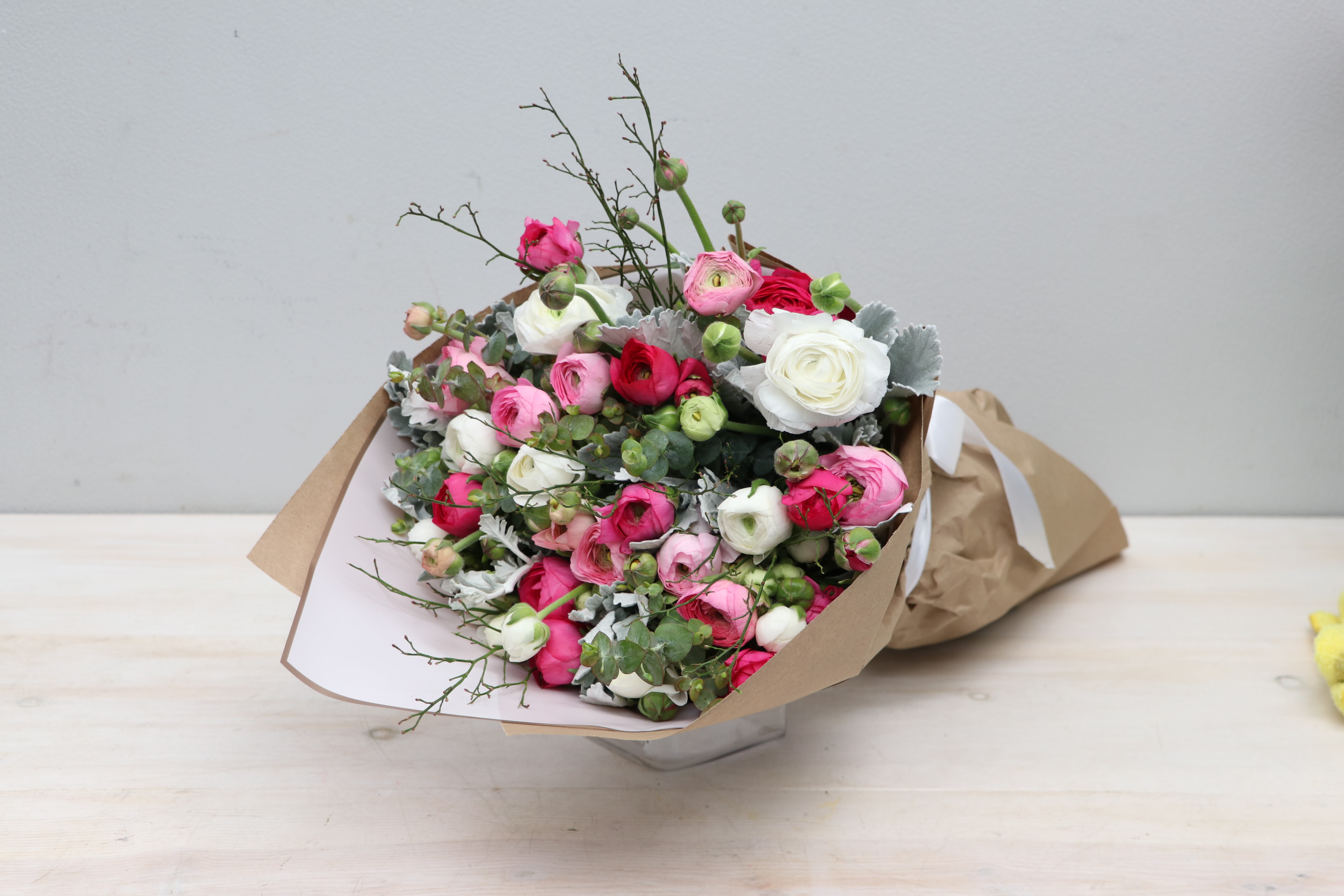 Bouquet of pink, white, and red ranunculus wrapped in brown paper