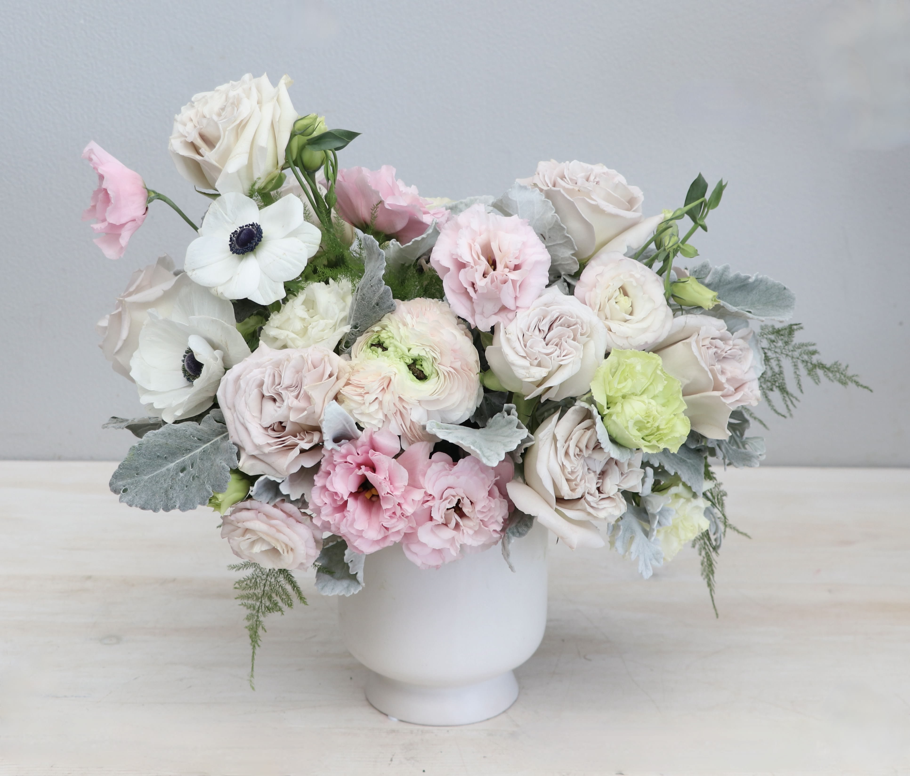 Pastel arrangement of roses, ranunculus, and anemones in a white pedestal vase