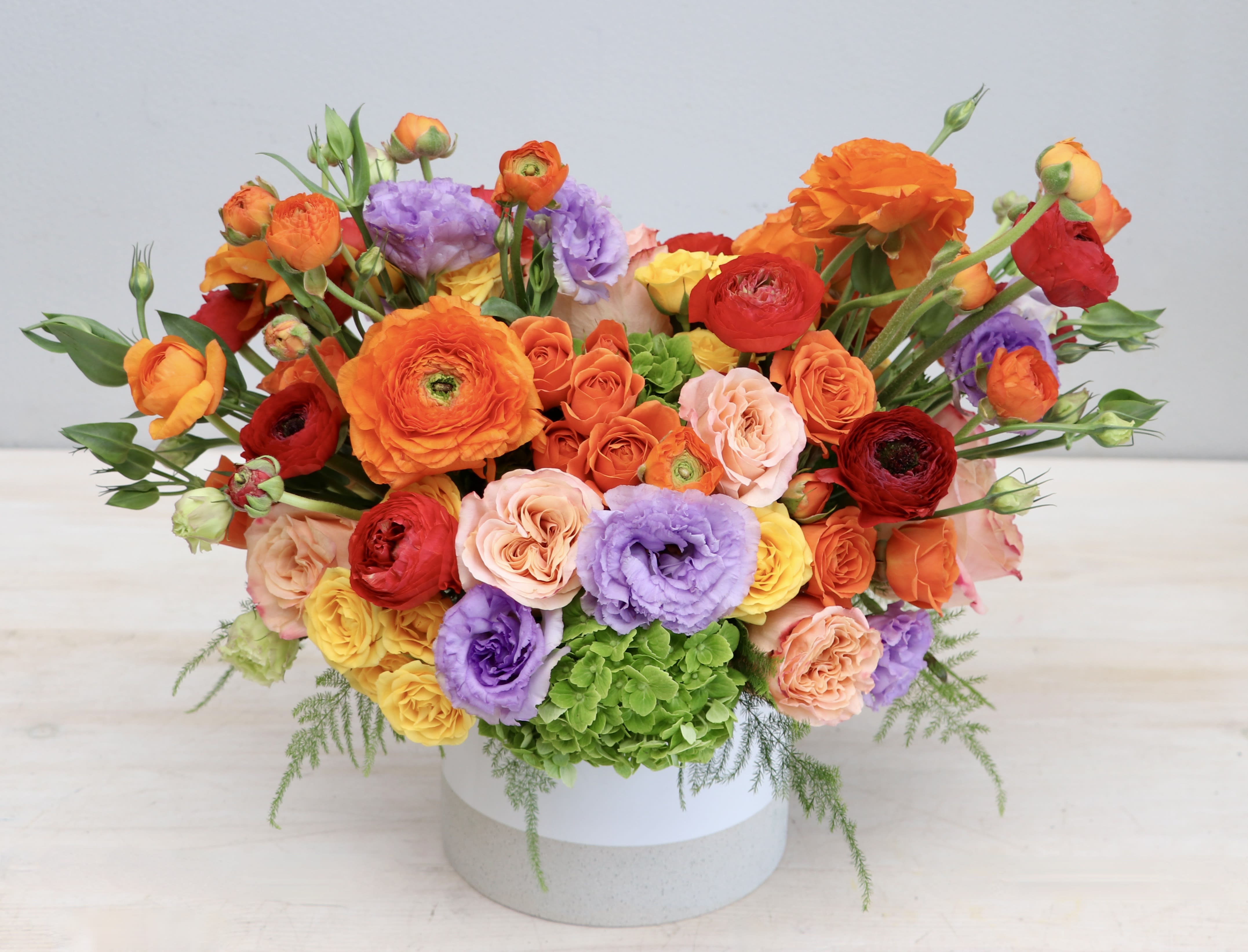Low white vase filled with bright orange, red, yellow, and purple flowers in a wide arrangement