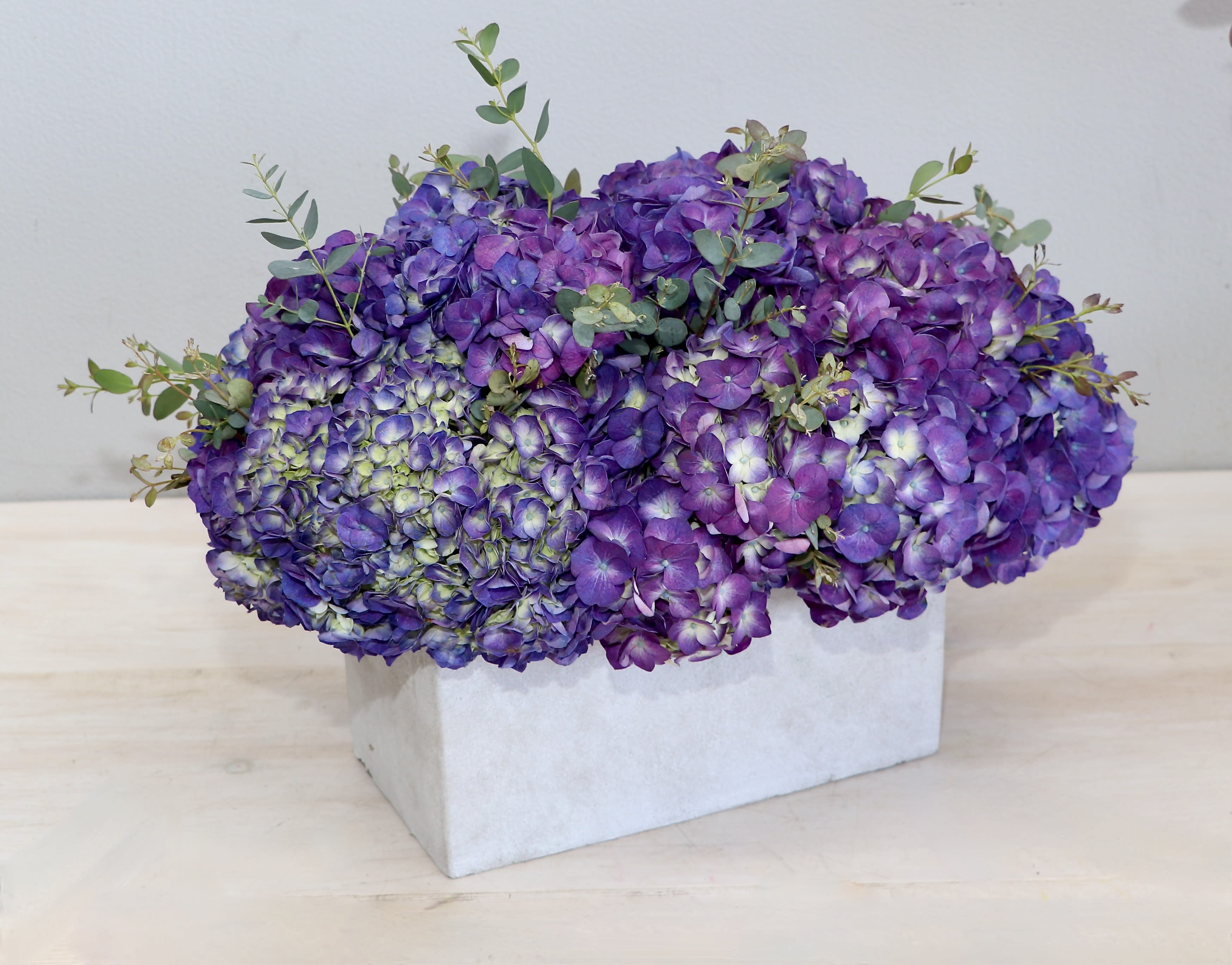Low arrangement of purple hydrangeas in a rectangular white box vase