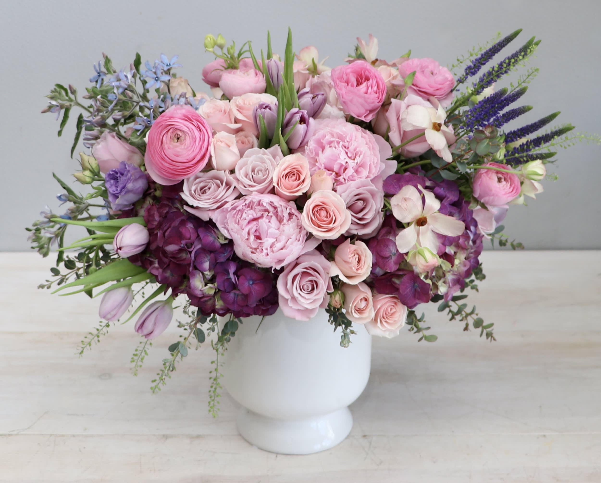 Low pink and purple flower arrangement with roses and peonies in a white ceramic vase.