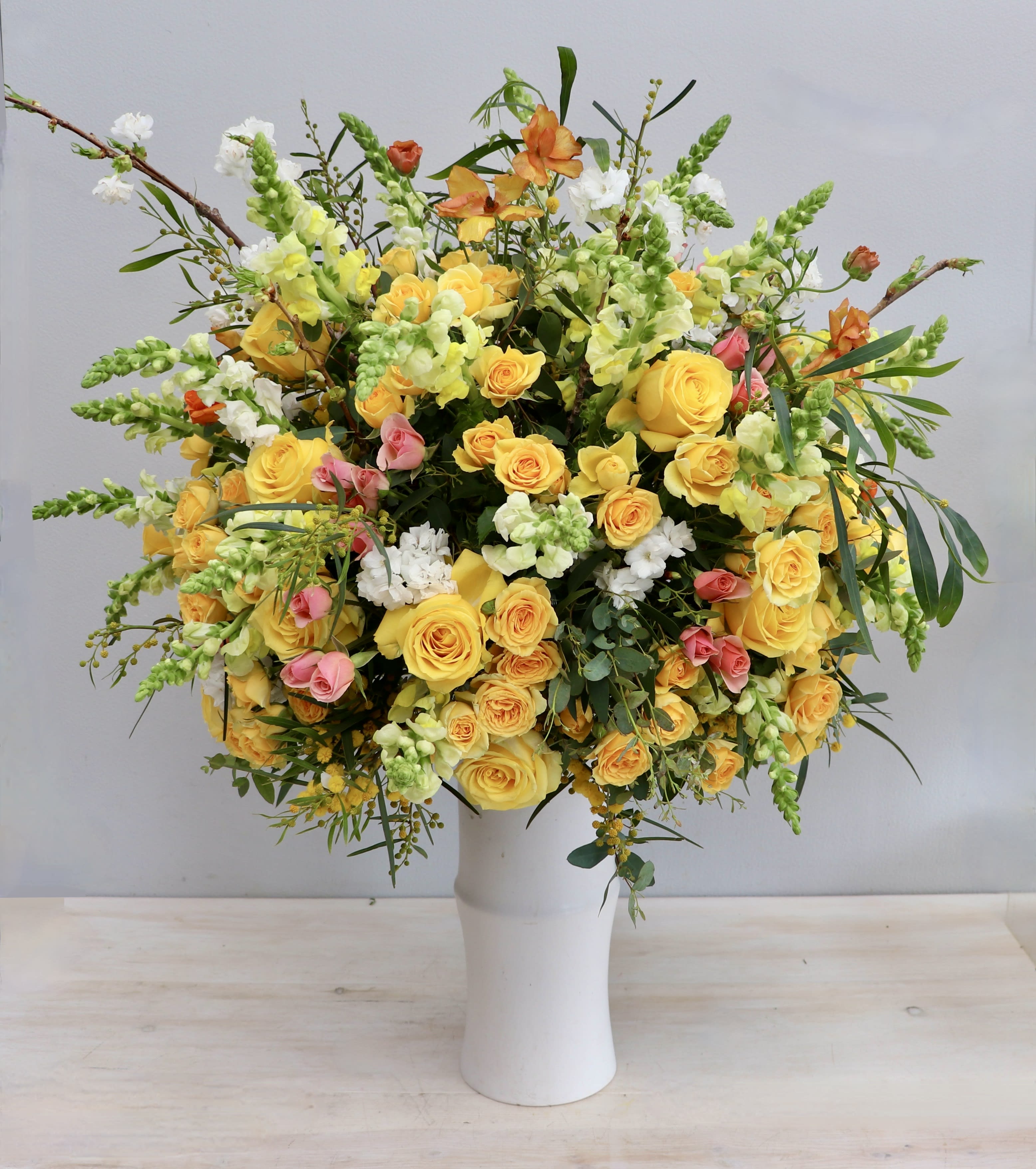 Tall arrangement of yellow roses with white and pink flowers in a white vase