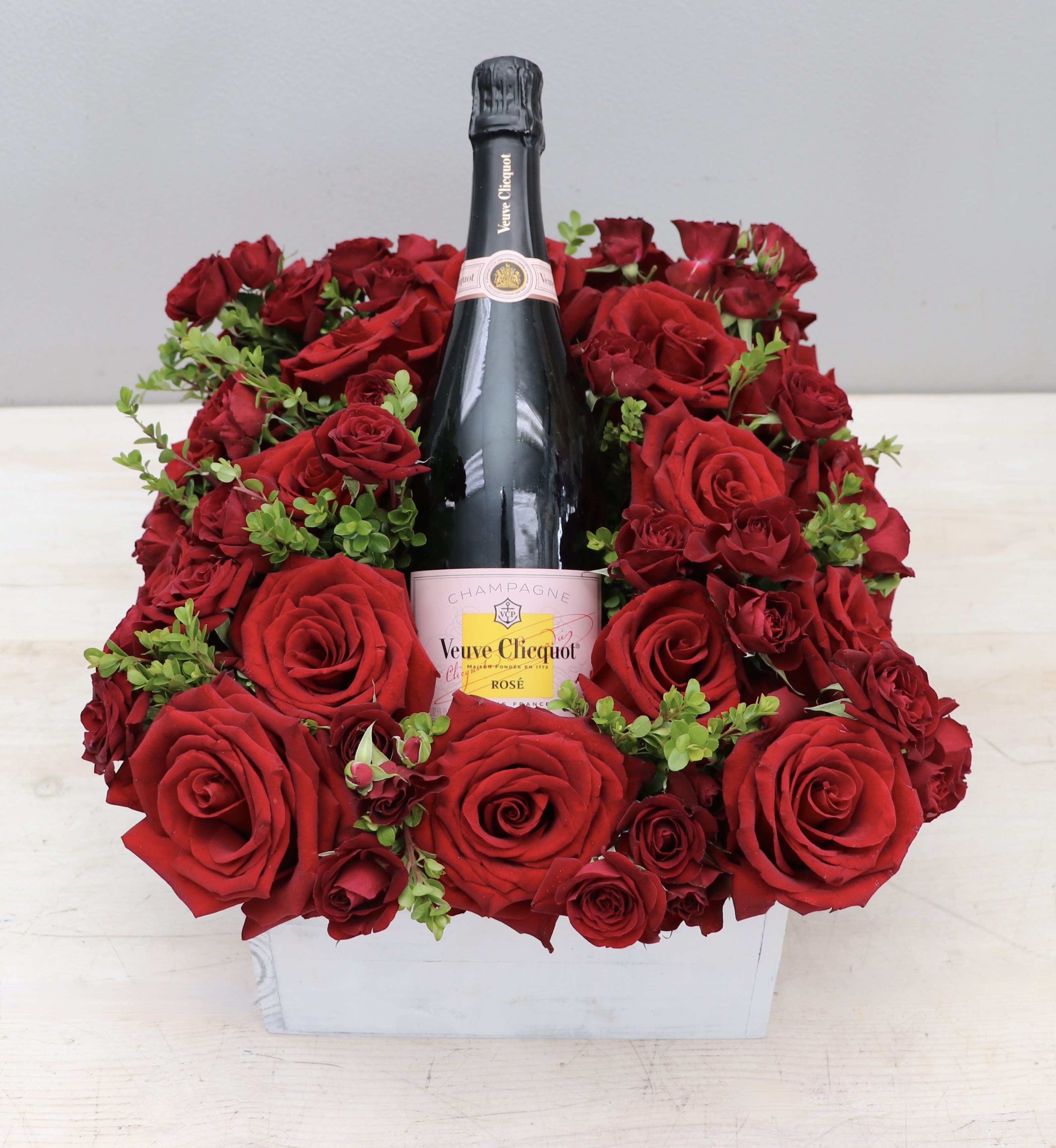 Bottle of rosé champagne surrounded by red roses in a white wooden box