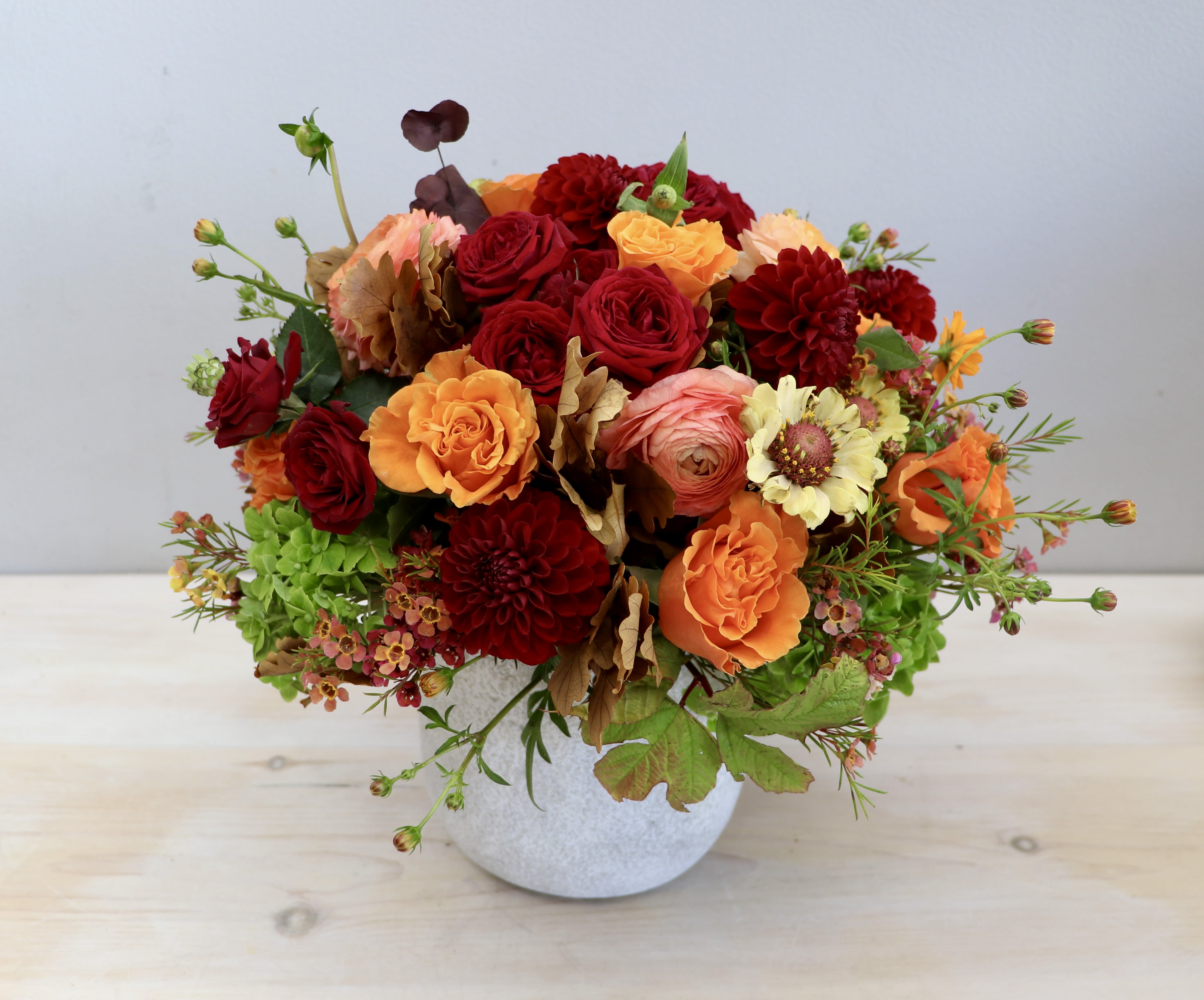 Low arrangement of red, orange, and yellow flowers in a white ceramic pot