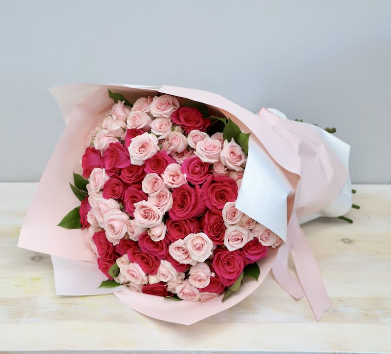 Large bouquet of light and hot pink roses wrapped in pale pink and white paper with ribbon