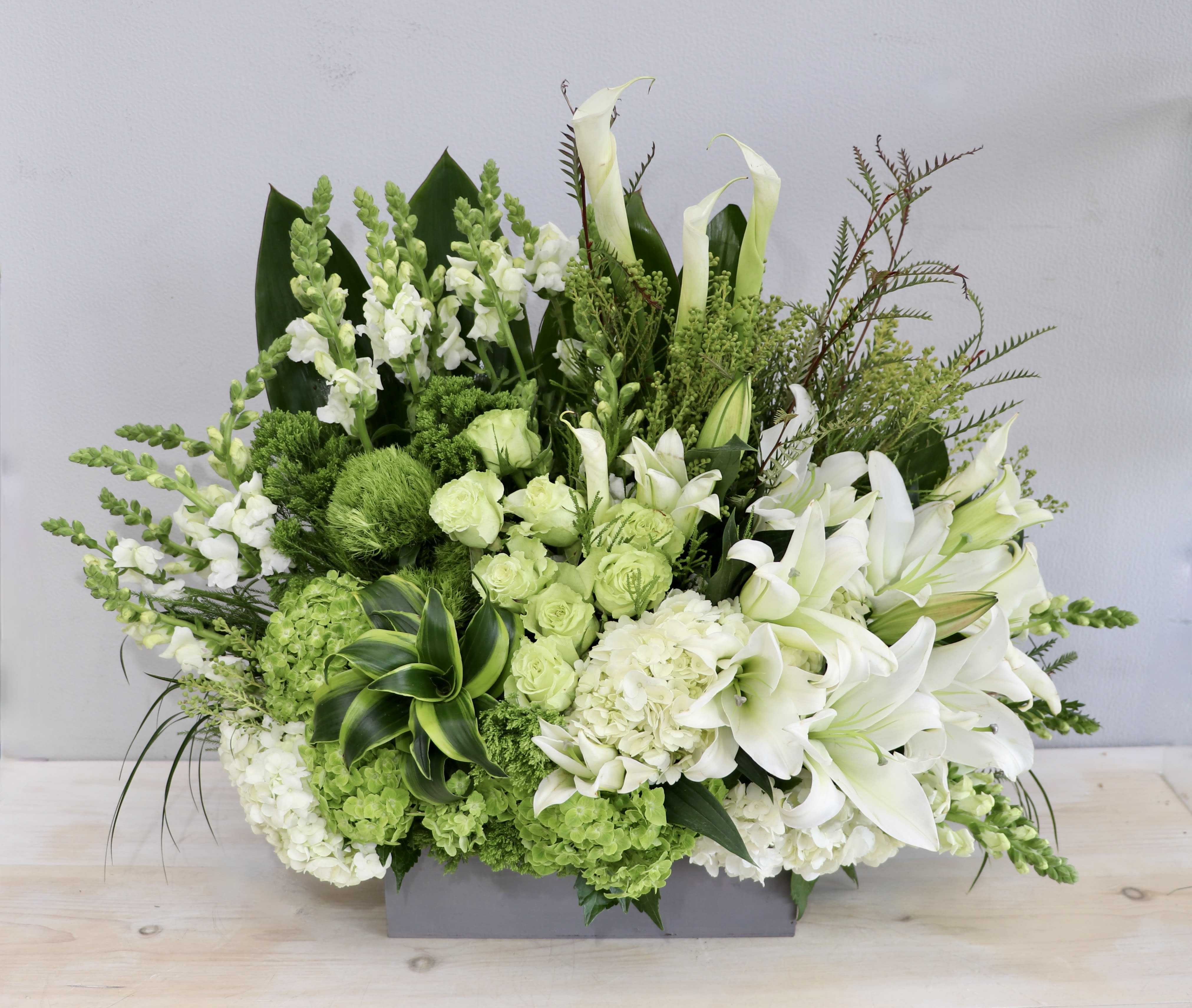 Large white and green arrangement with lilies and hydrangeas in a low gray rectangular container