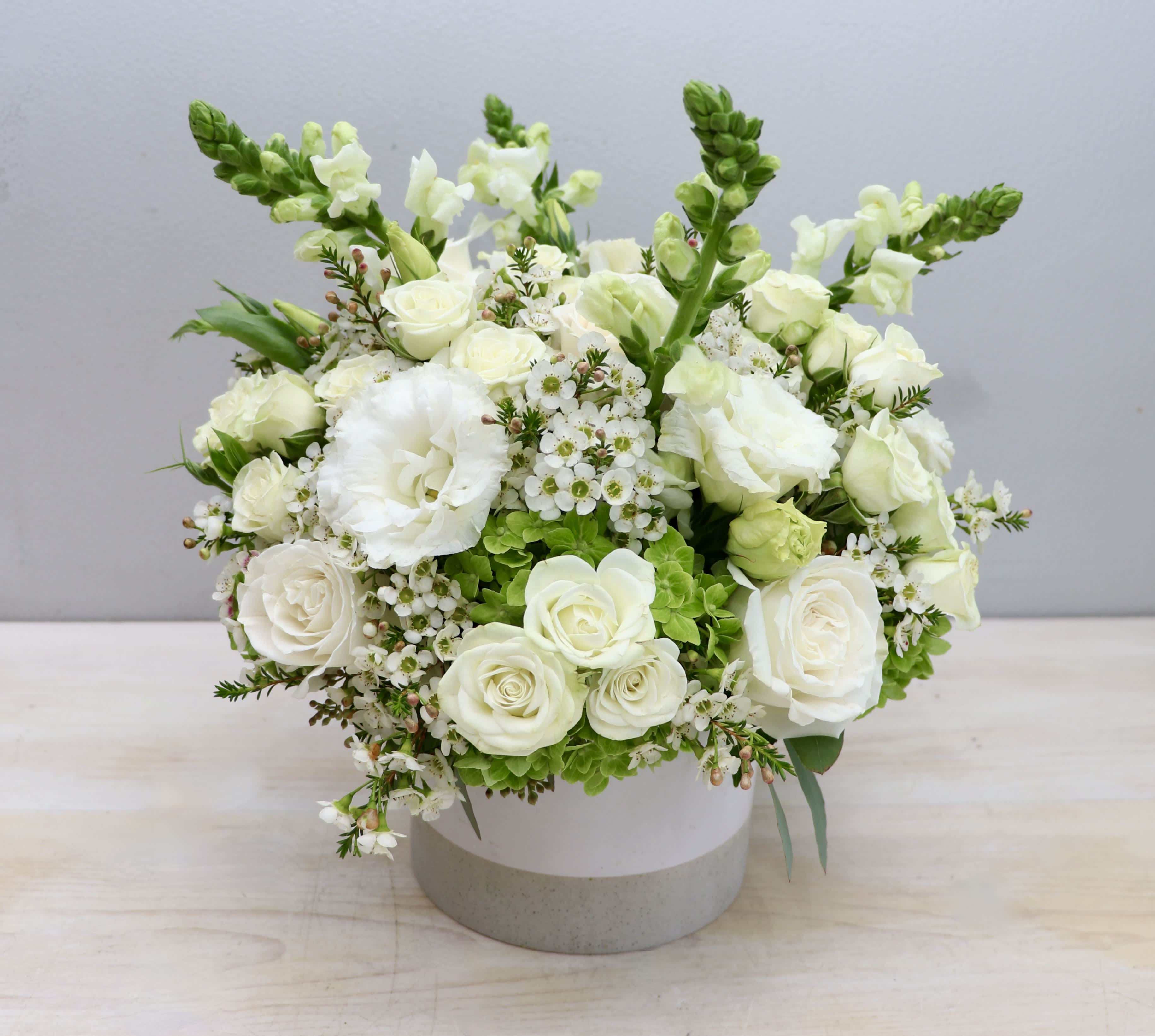 Round white flower arrangement with roses and snapdragons in a white ceramic vase
