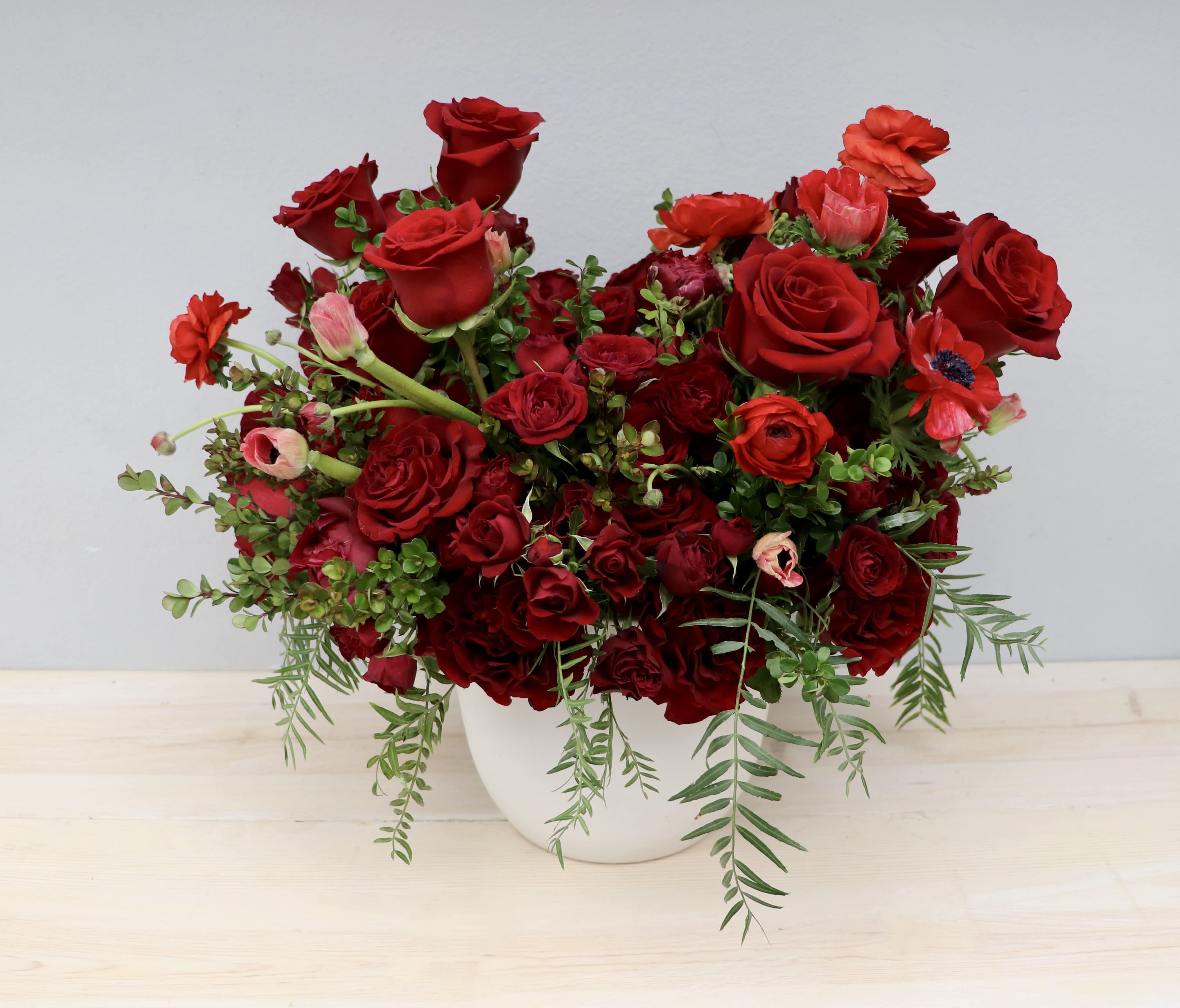Lush arrangement of deep red roses and mixed red blooms in a white round vase