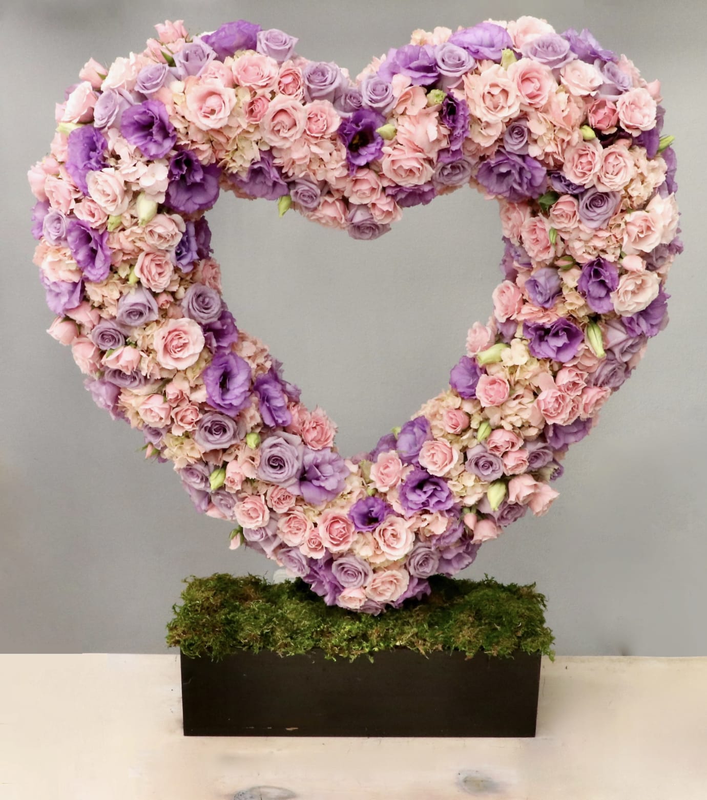 Large open heart of pink and purple flowers on a moss-covered rectangular base