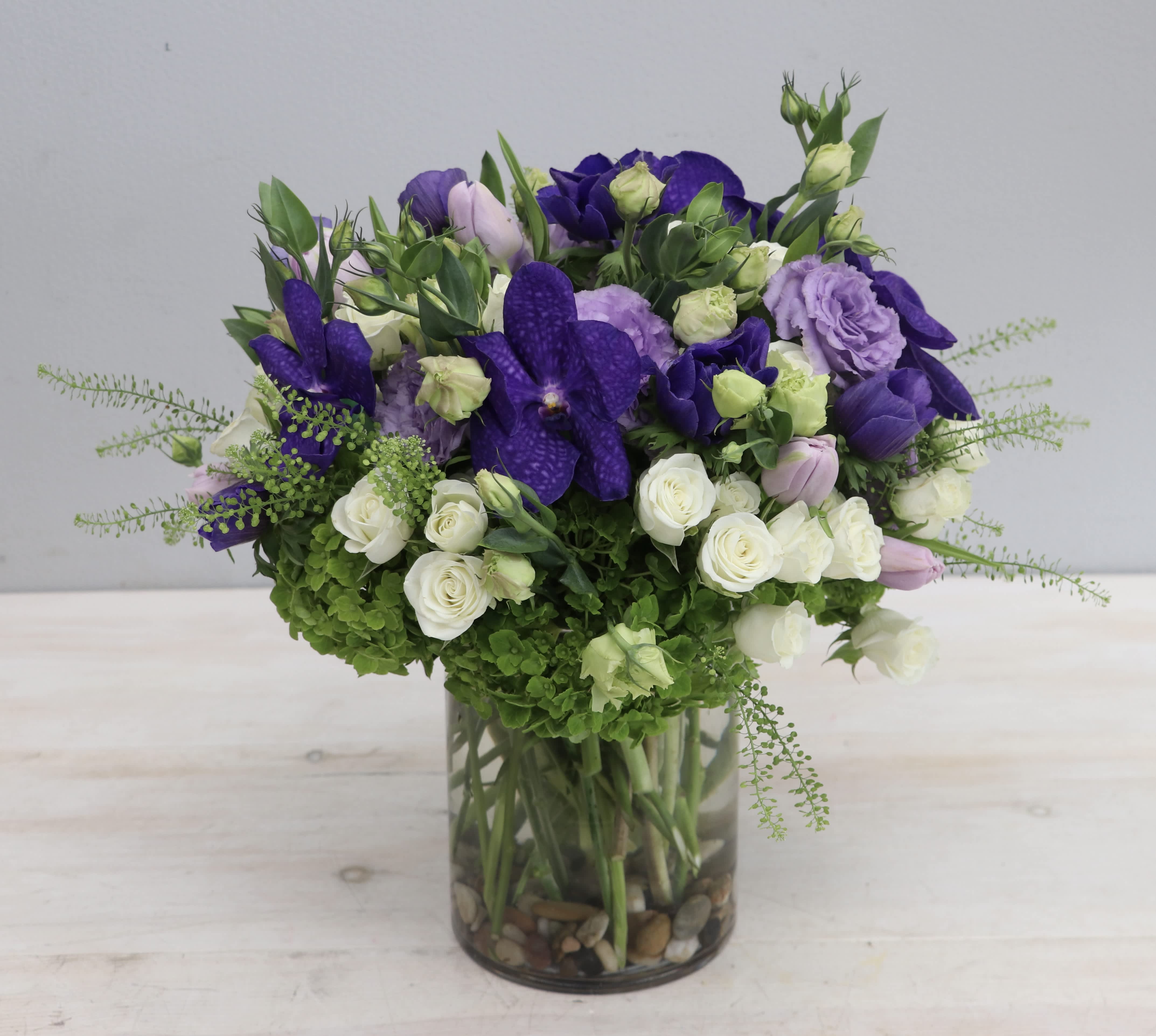 Round arrangement of purple and white flowers with green hydrangea in a clear glass cylinder vase
