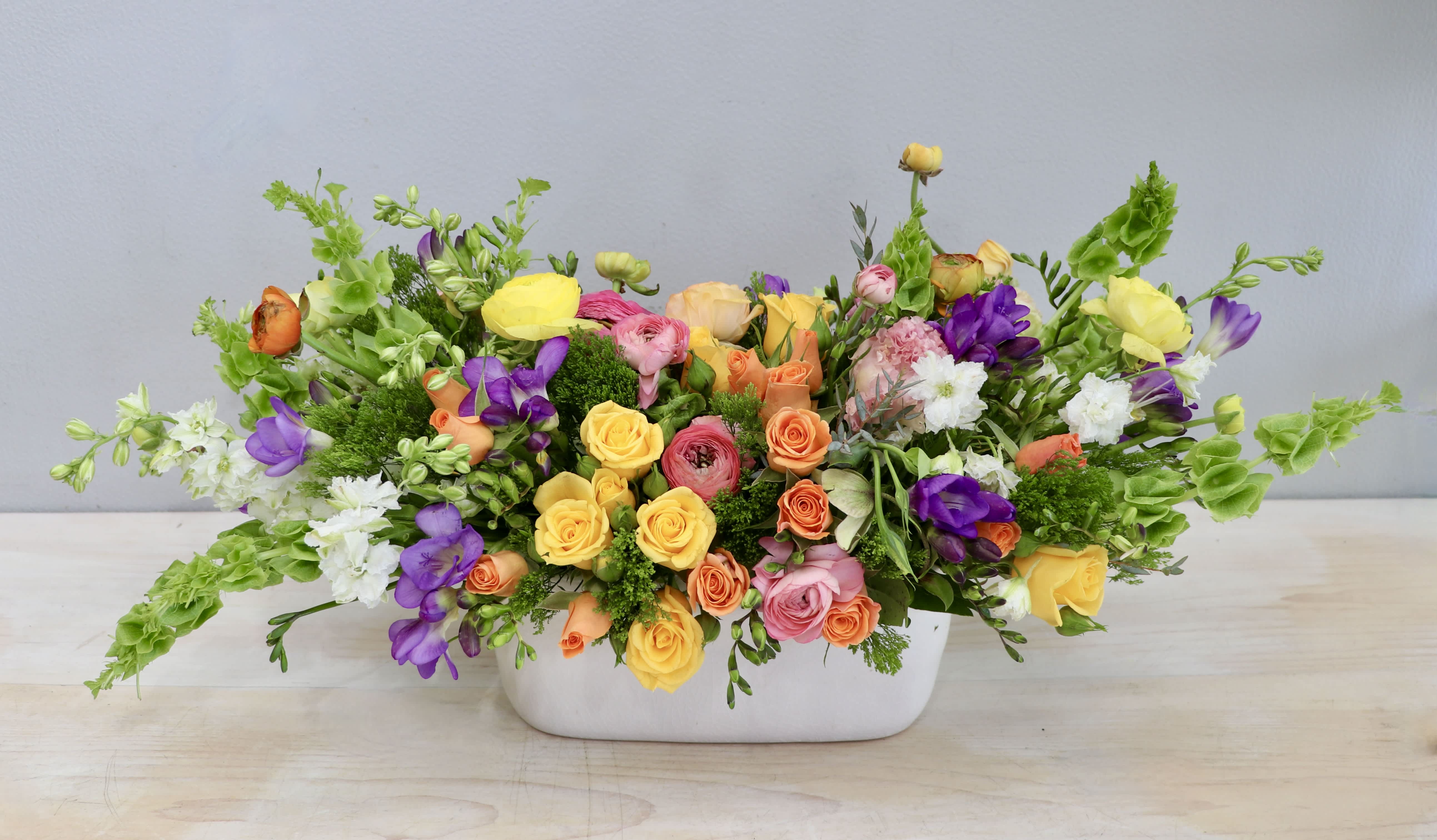 Low centerpiece of yellow, pink, orange, and purple flowers in a white rectangular container