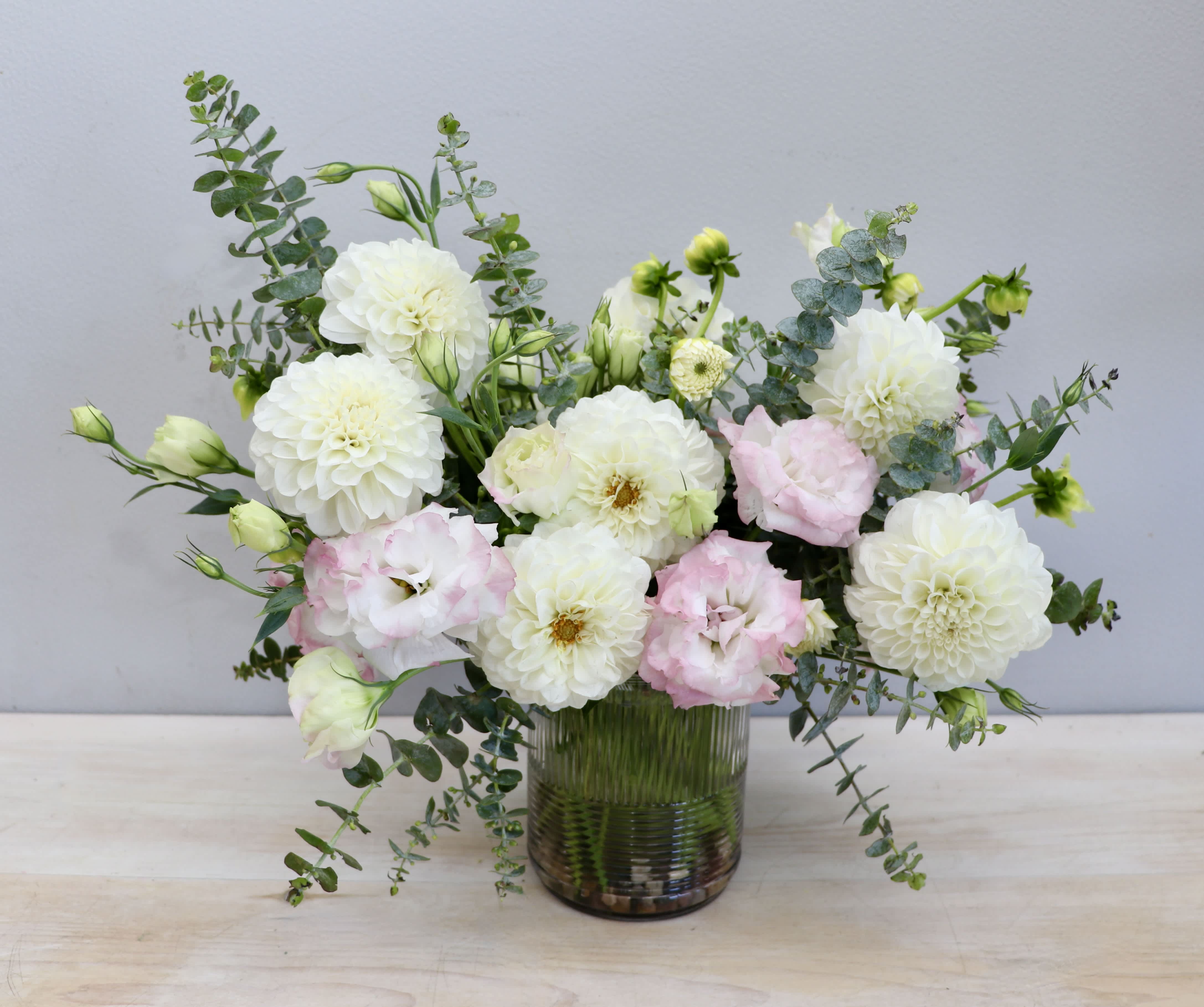Low glass vase of white dahlias and pale pink lisianthus with airy greenery.
