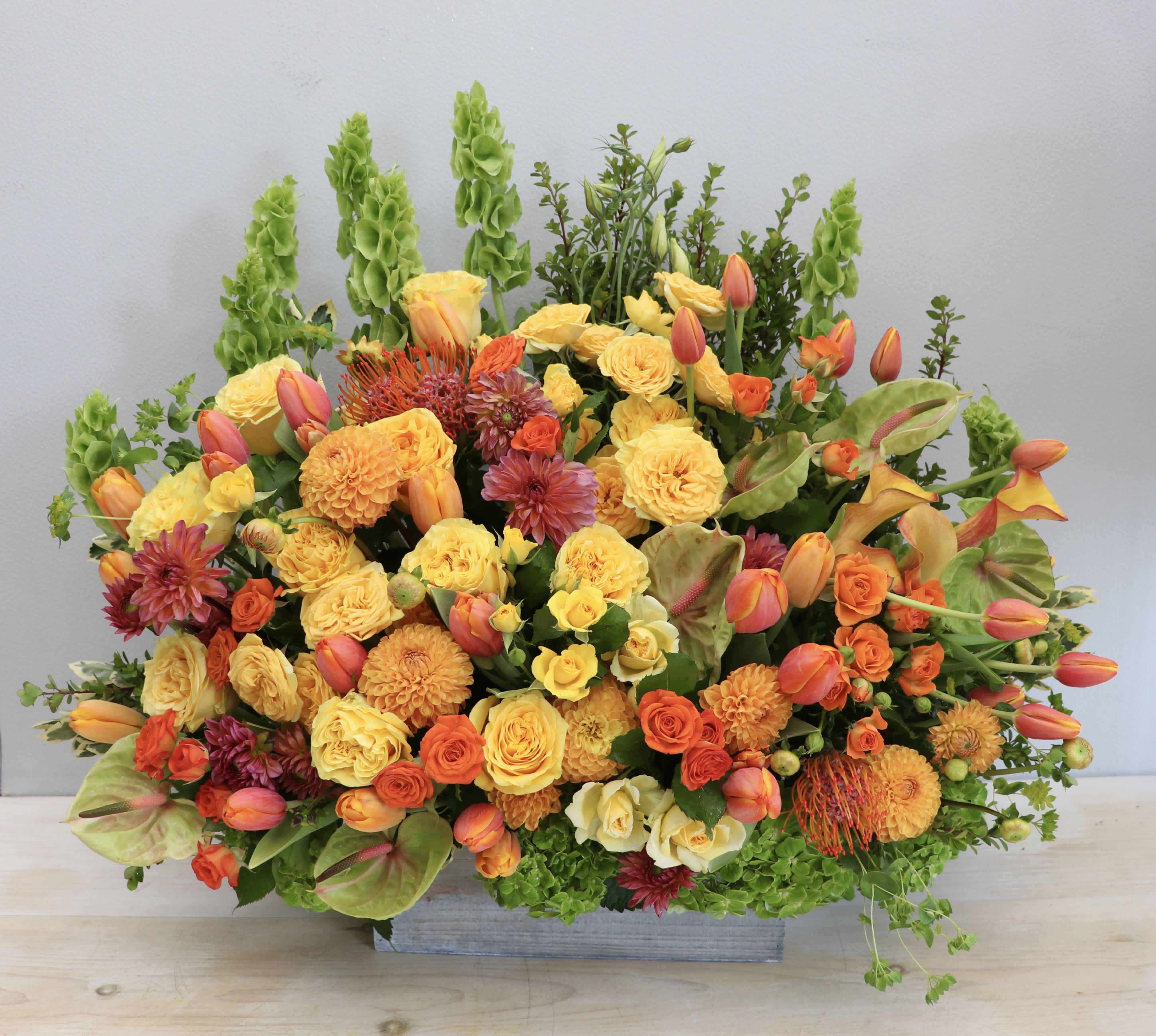 Tall yellow and orange floral arrangement with roses, tulips, and mums in a rectangular container