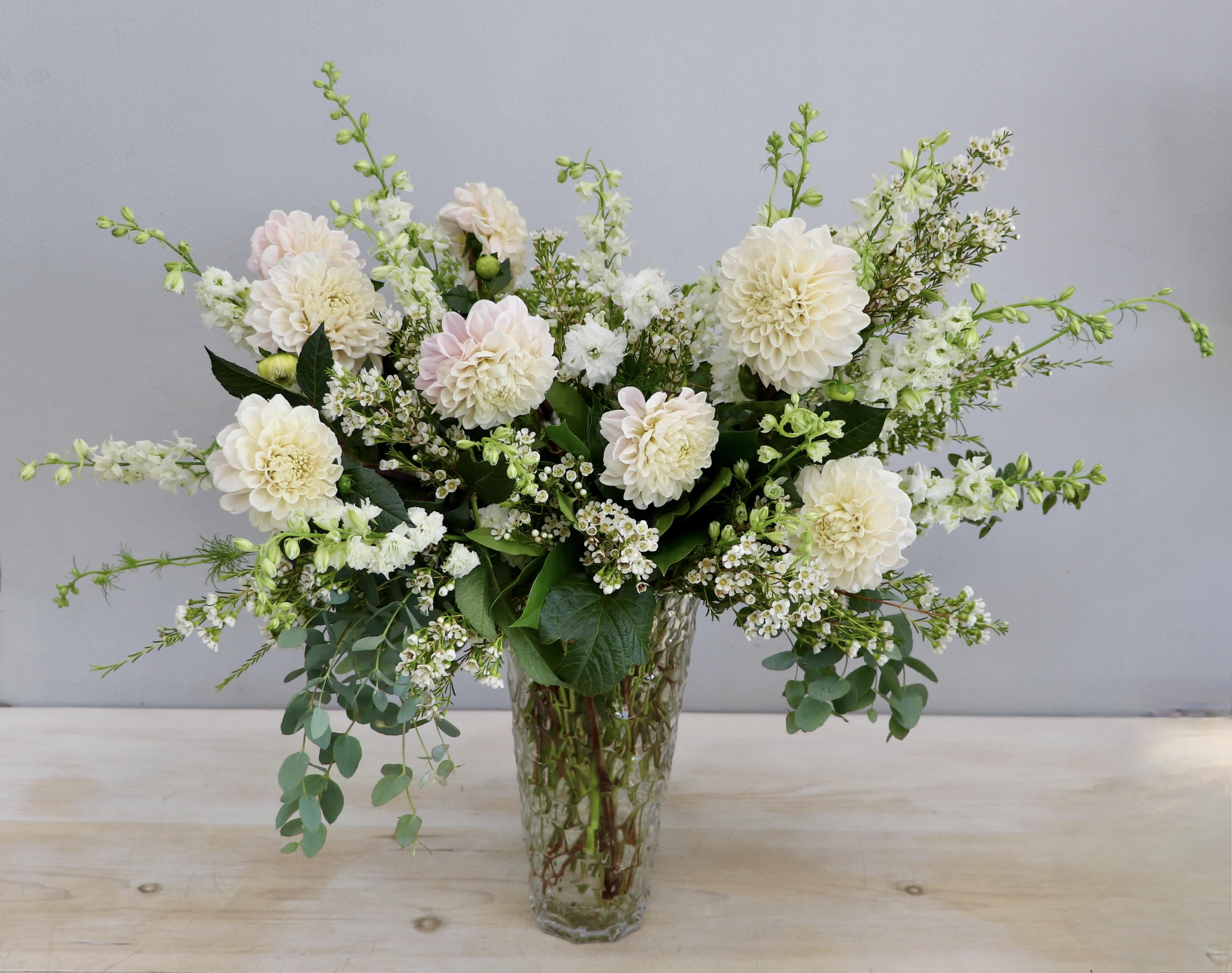 Tall arrangement of cream dahlias and white flowers in a clear textured glass vase