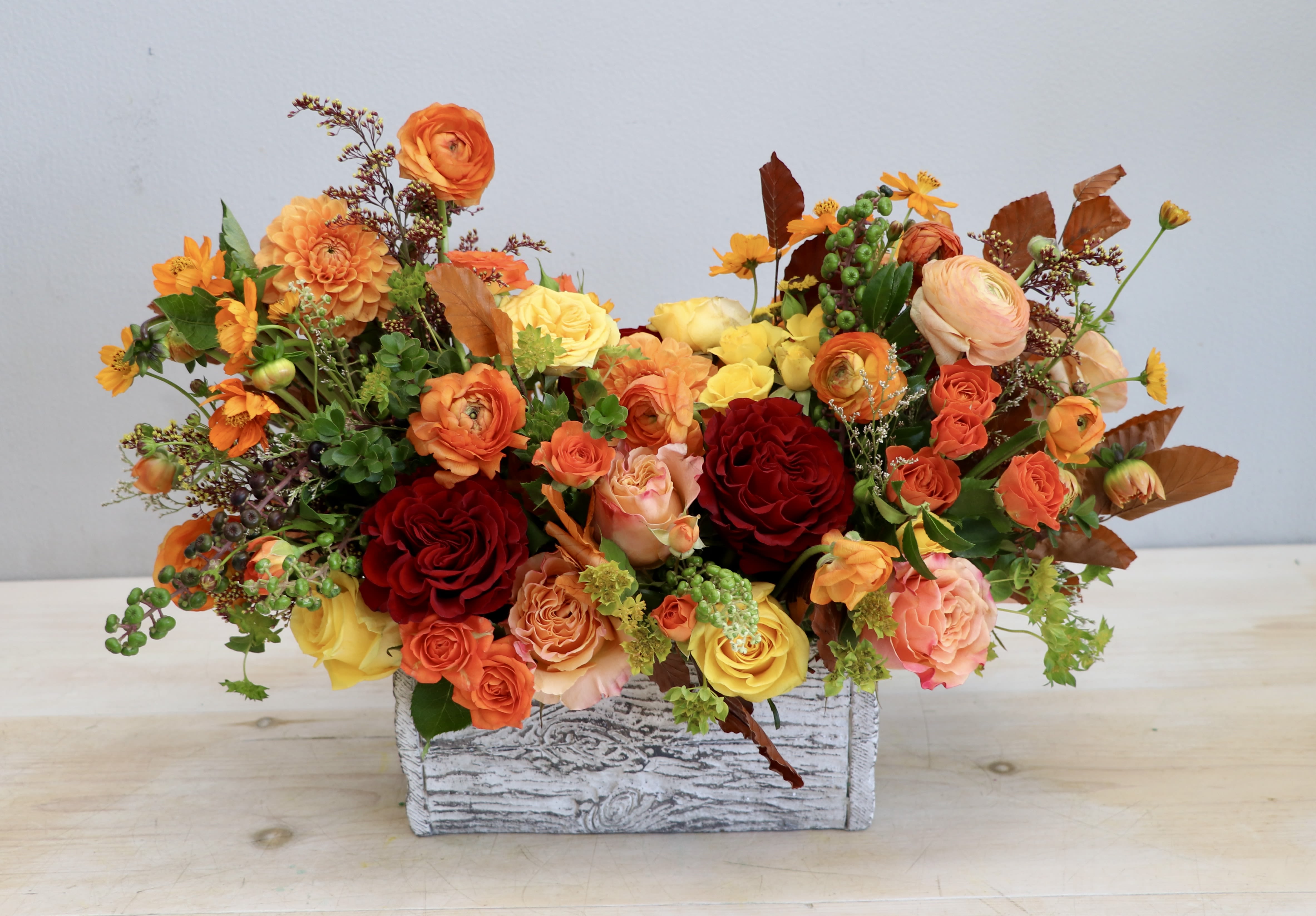 Low autumn-toned arrangement of orange, yellow, and red flowers in a whitewashed wooden box