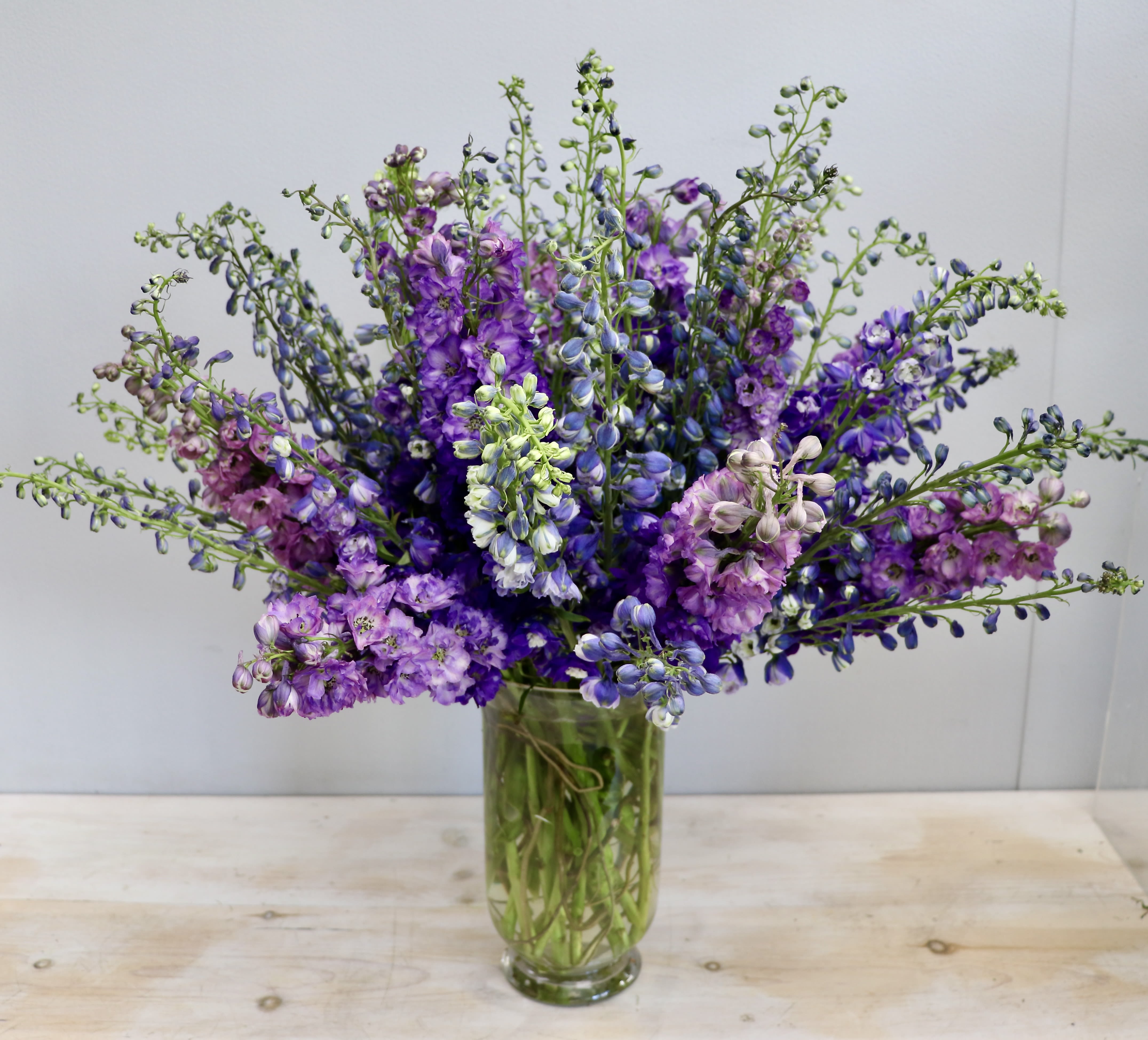 Tall arrangement of purple and blue delphinium in a clear glass cylinder vase