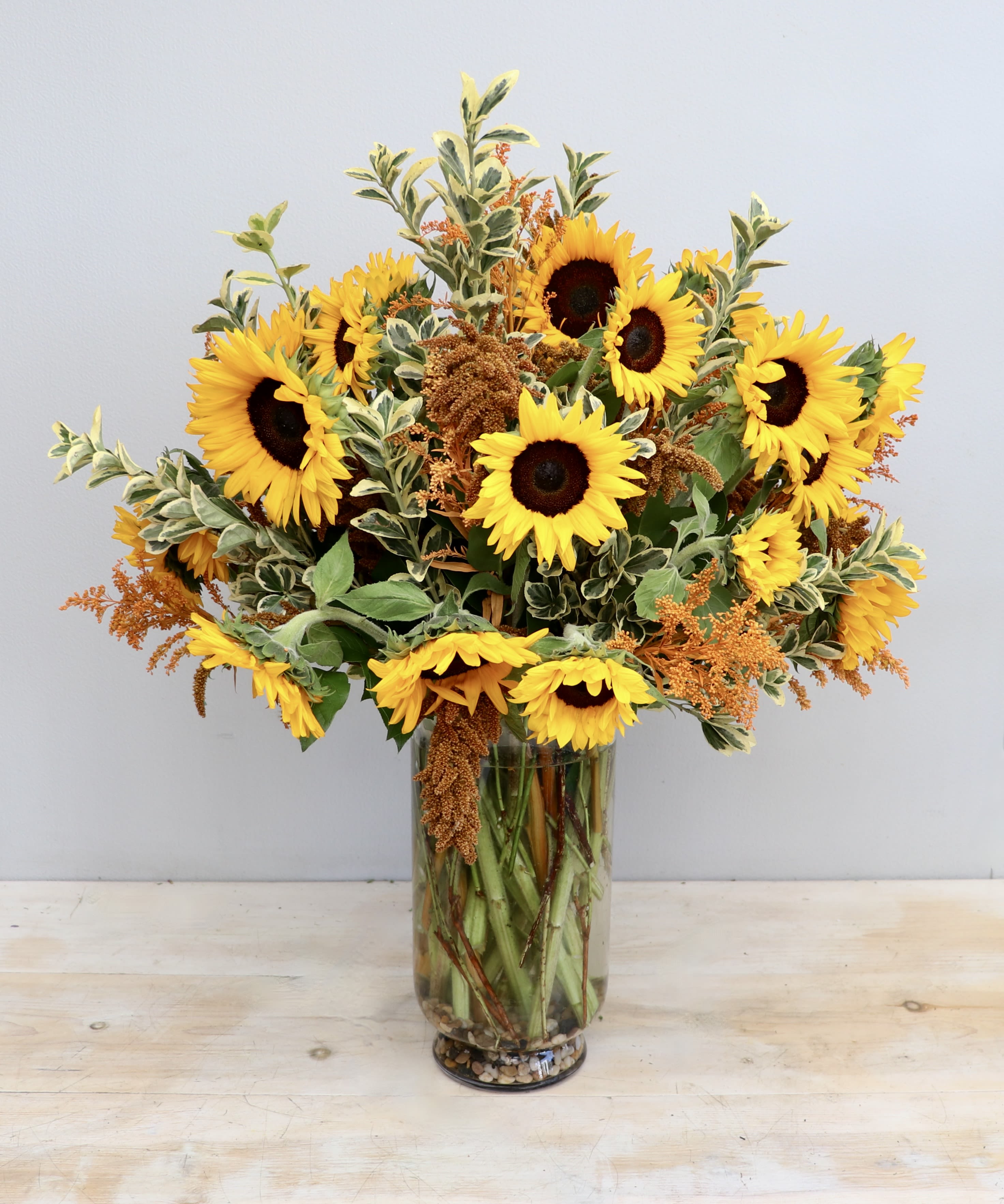 Tall glass vase of yellow sunflowers with orange filler blooms and variegated foliage