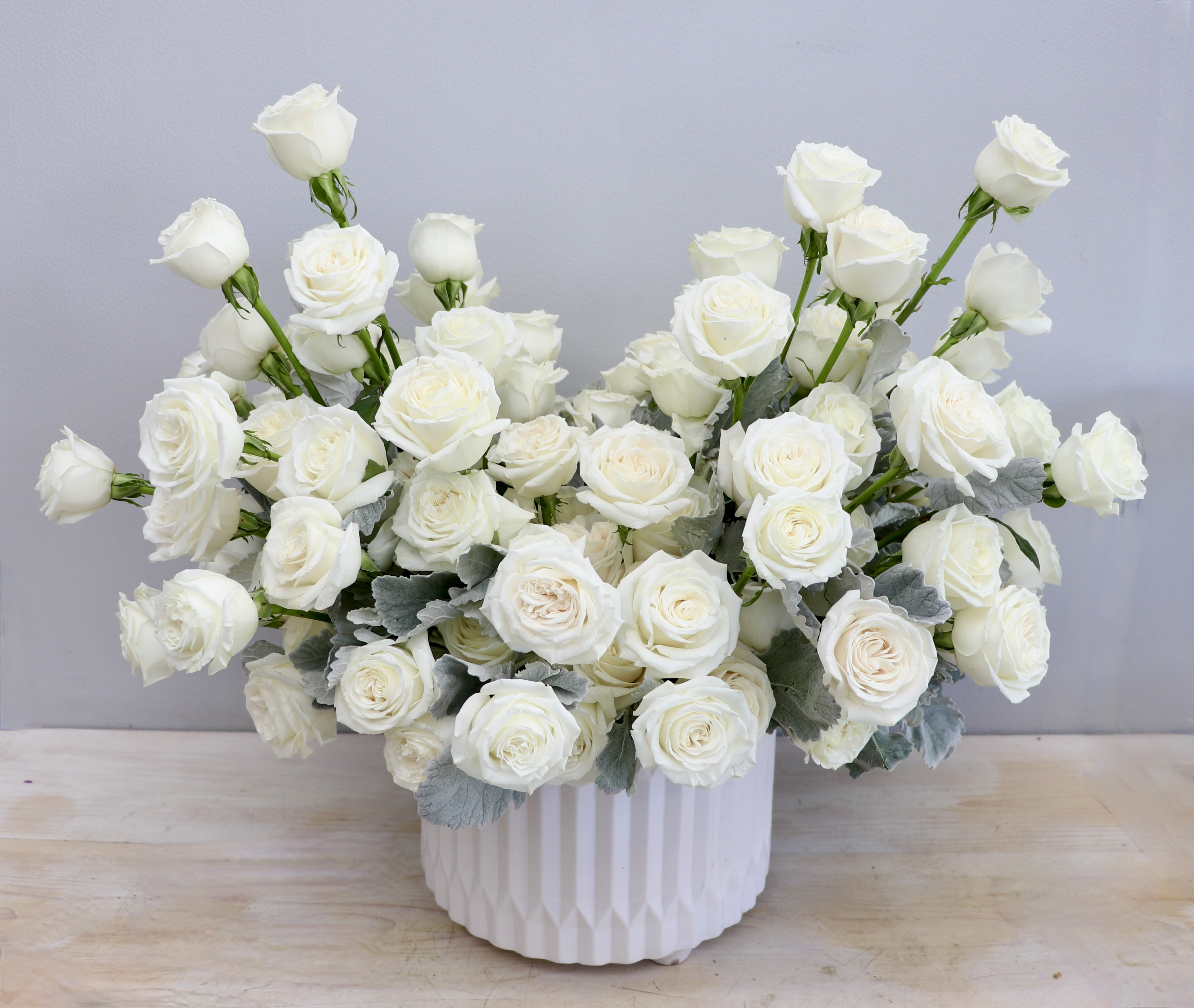 Low arrangement of white roses in a white ceramic container.