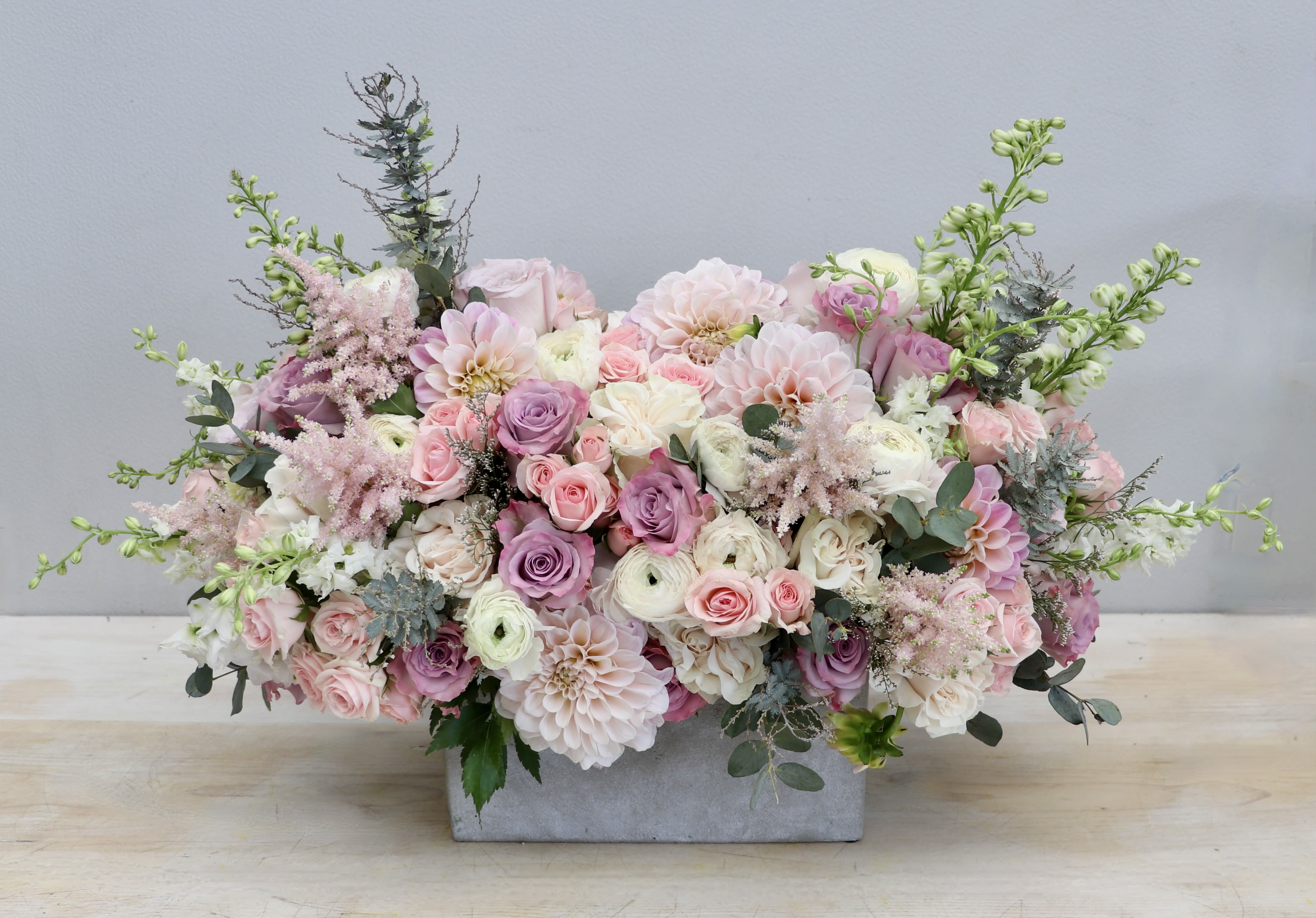 Low pastel arrangement of roses, dahlias, and ranunculus in a rectangular stone container