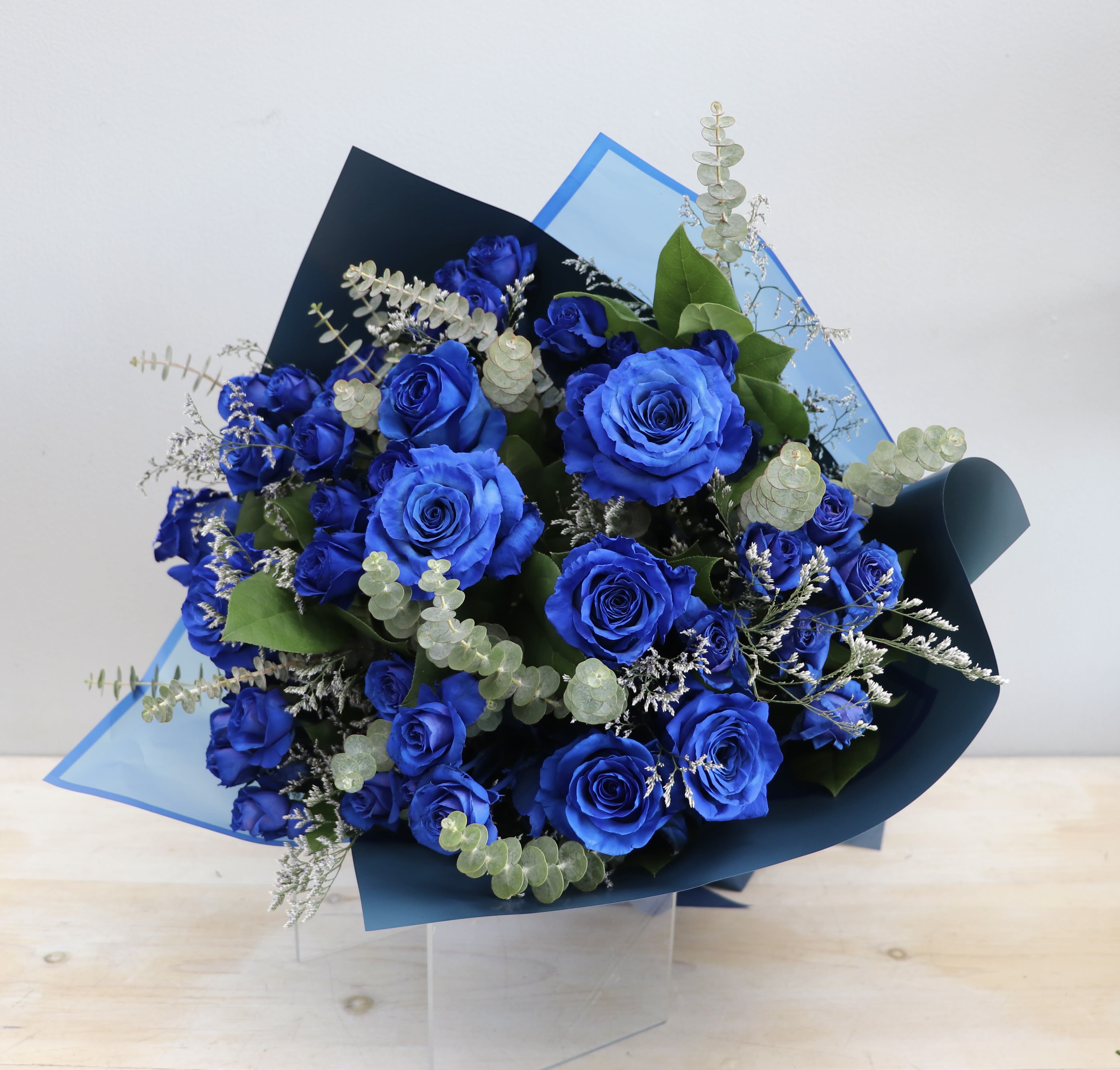 Hand-tied bouquet of vivid blue roses with silver eucalyptus in blue wrapping paper