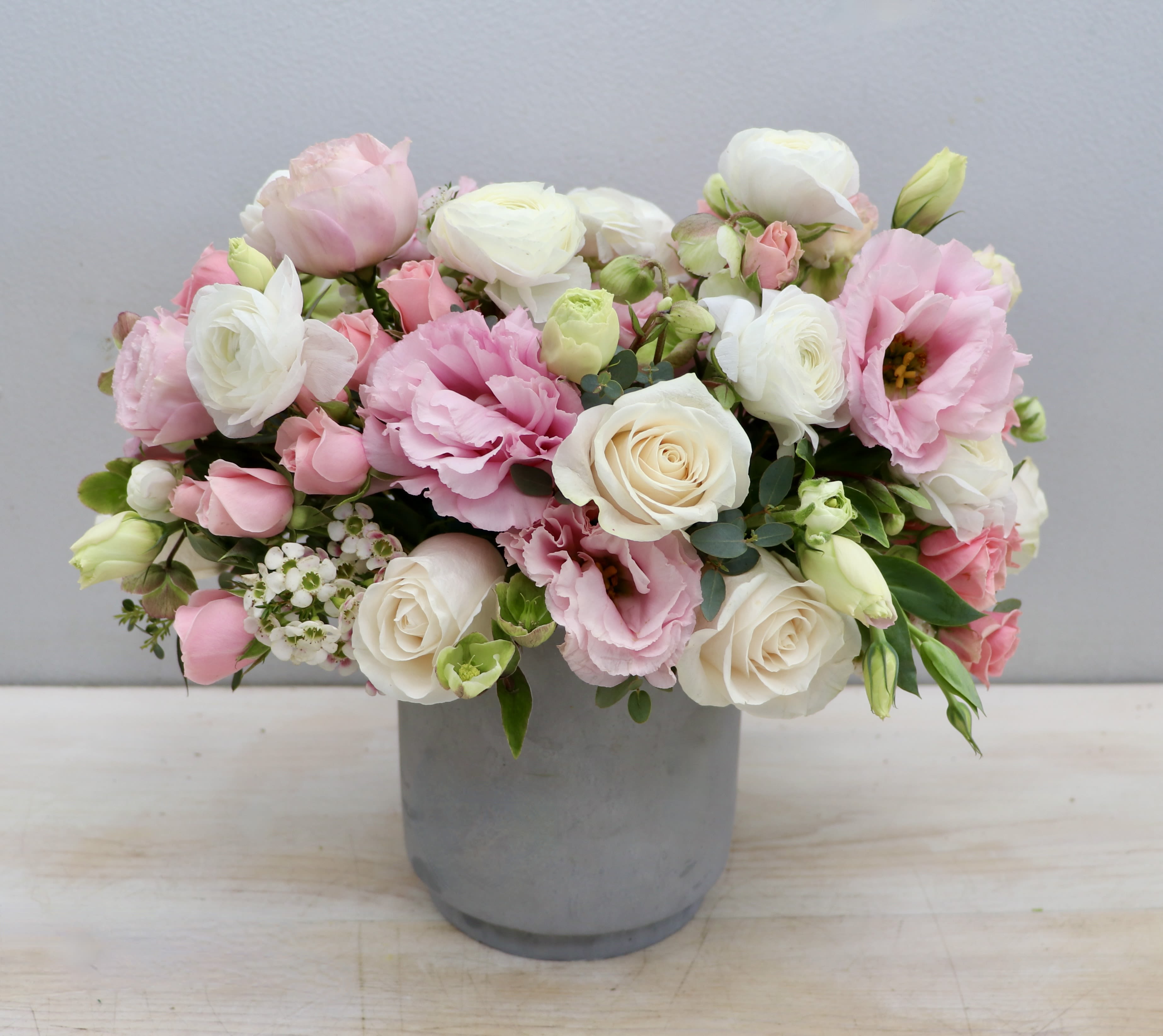 Low pastel arrangement of pink and white roses and lisianthus in a gray cylinder vase