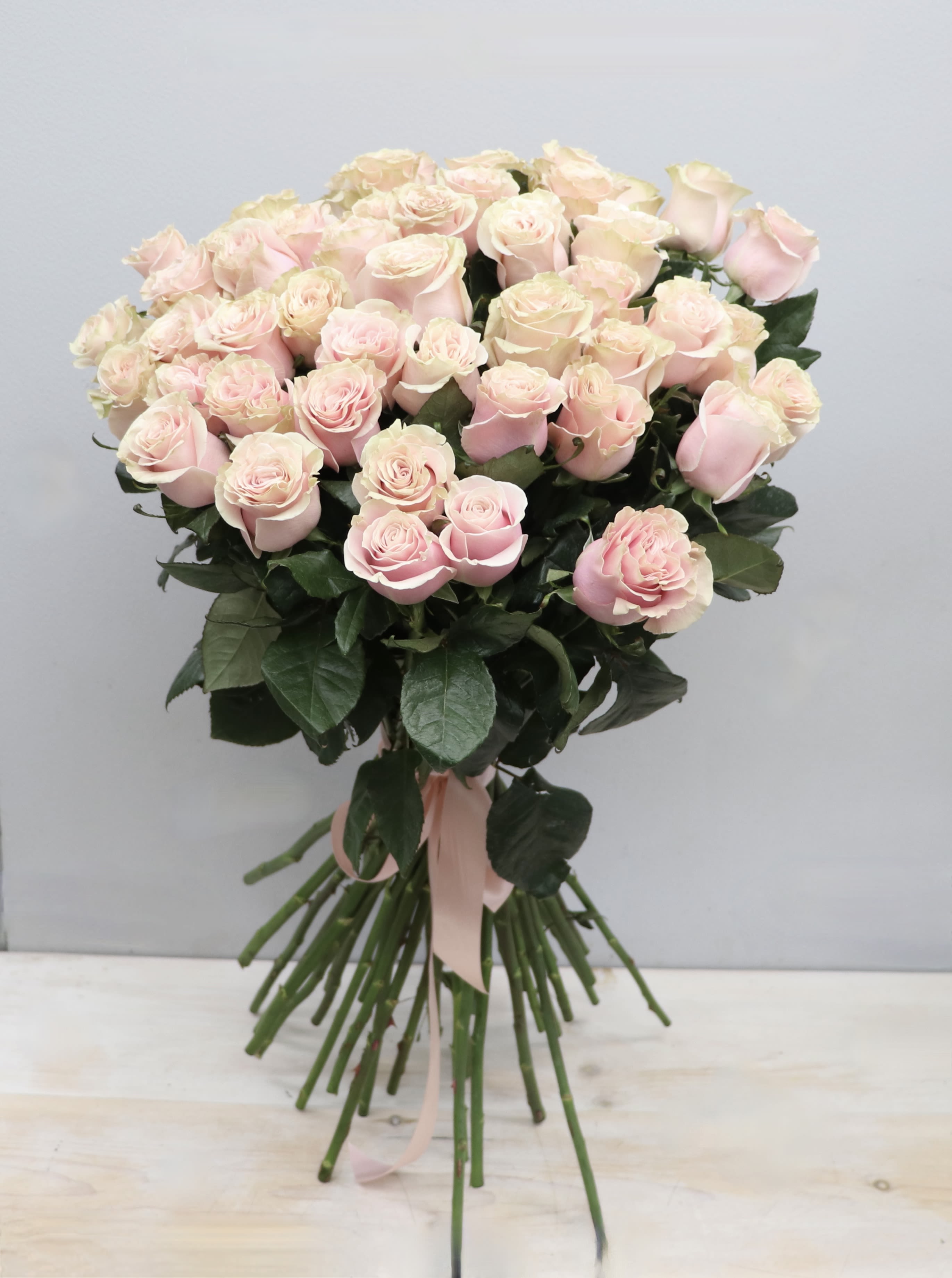 Large hand-tied bouquet of pale pink roses with long stems and a pink ribbon