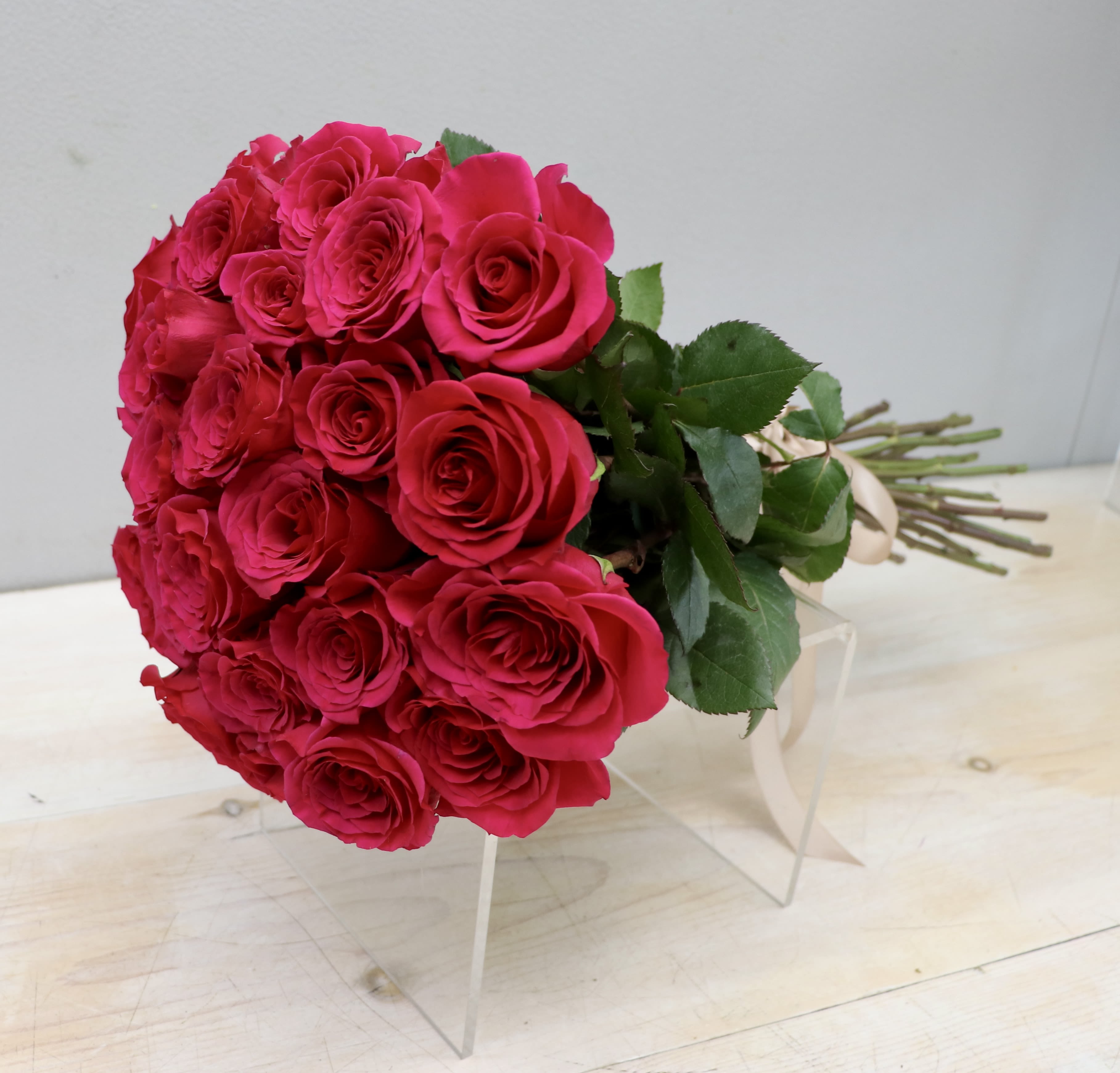 Hand-tied bouquet of hot pink roses with long stems and ribbon lying on a clear stand.
