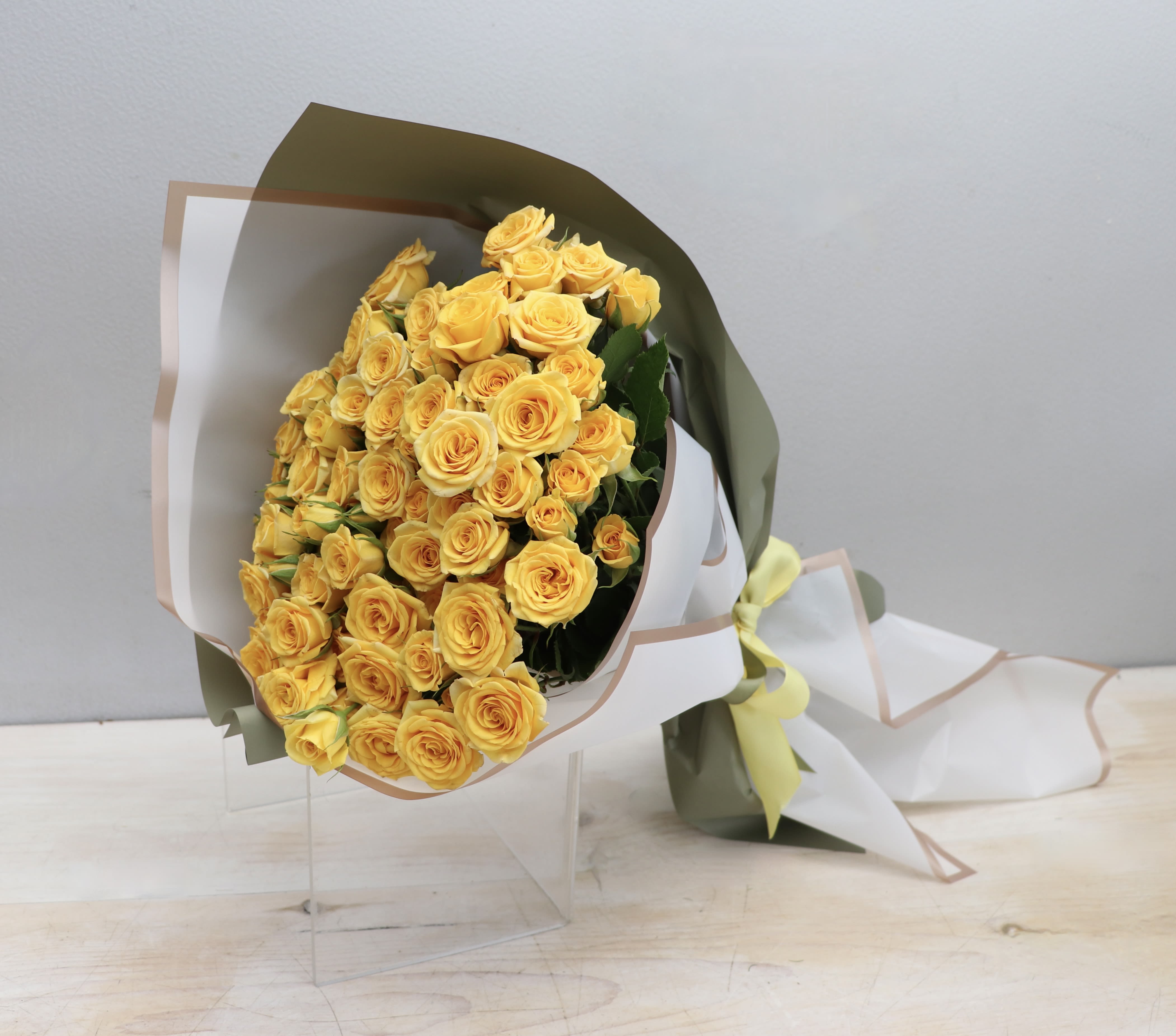 Large bouquet of clustered yellow roses wrapped in white and green paper with a bow
