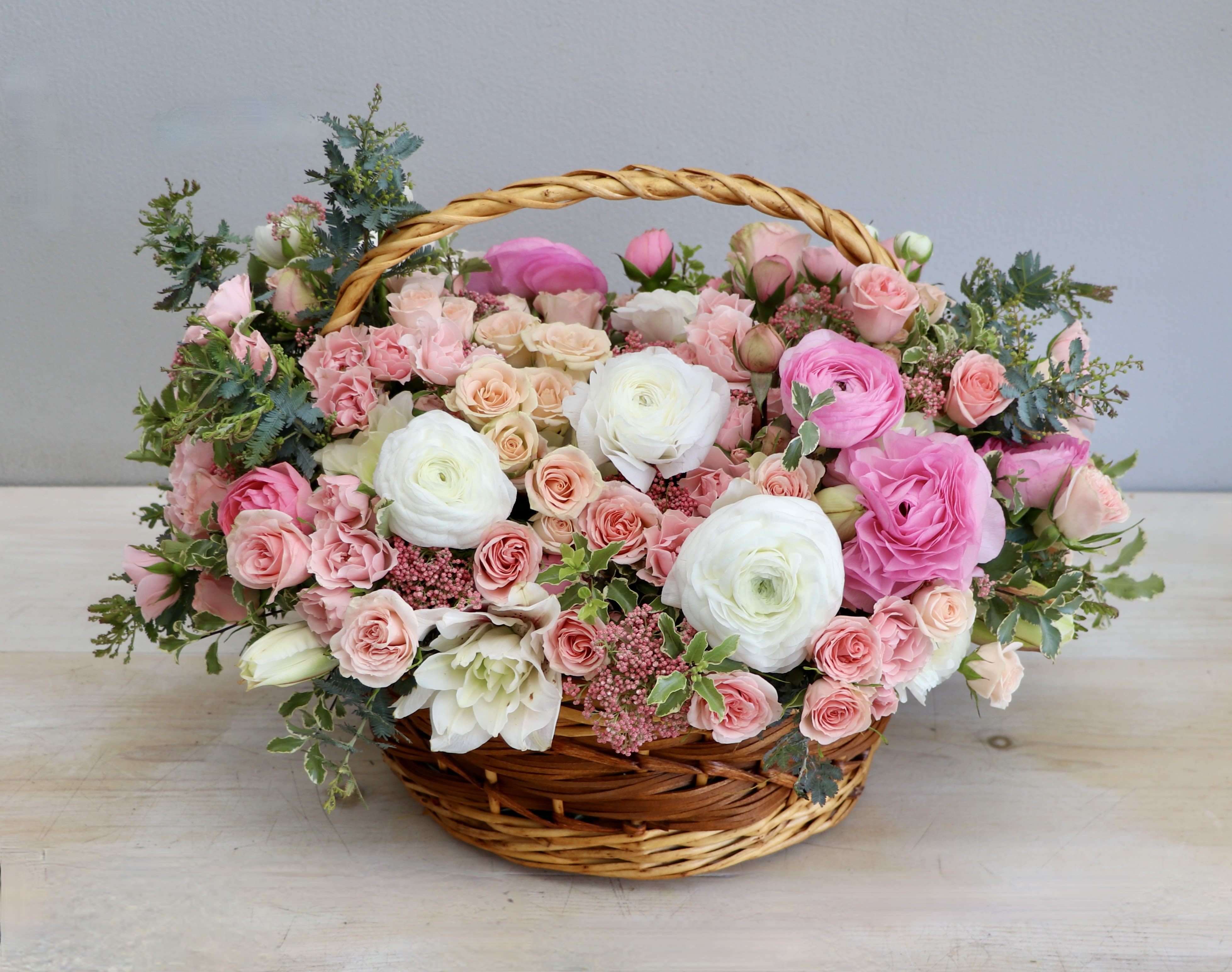 Low basket arrangement of pink and white roses and ranunculus in a woven wicker basket