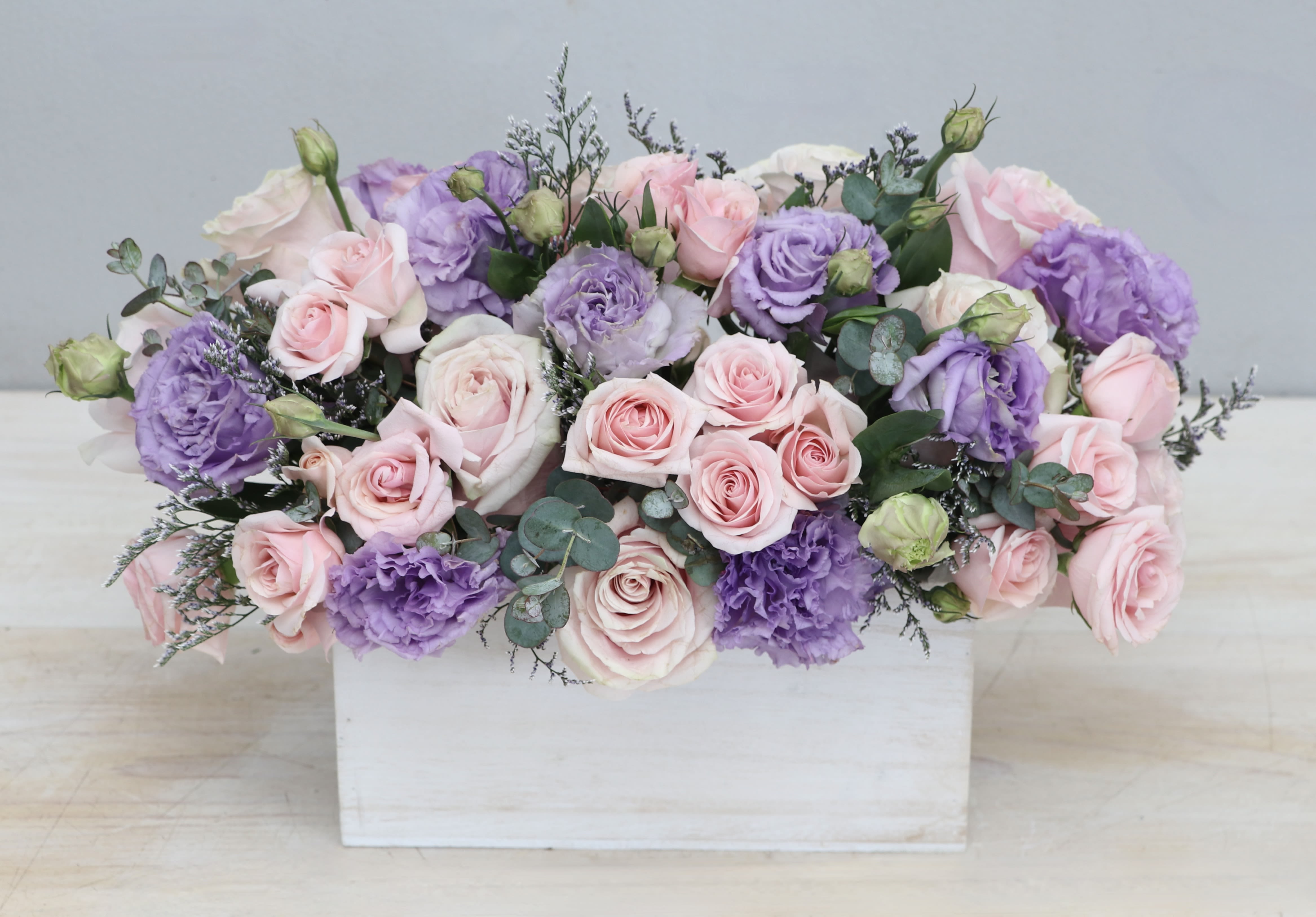 Low arrangement of pink roses and lavender lisianthus in a white wooden box