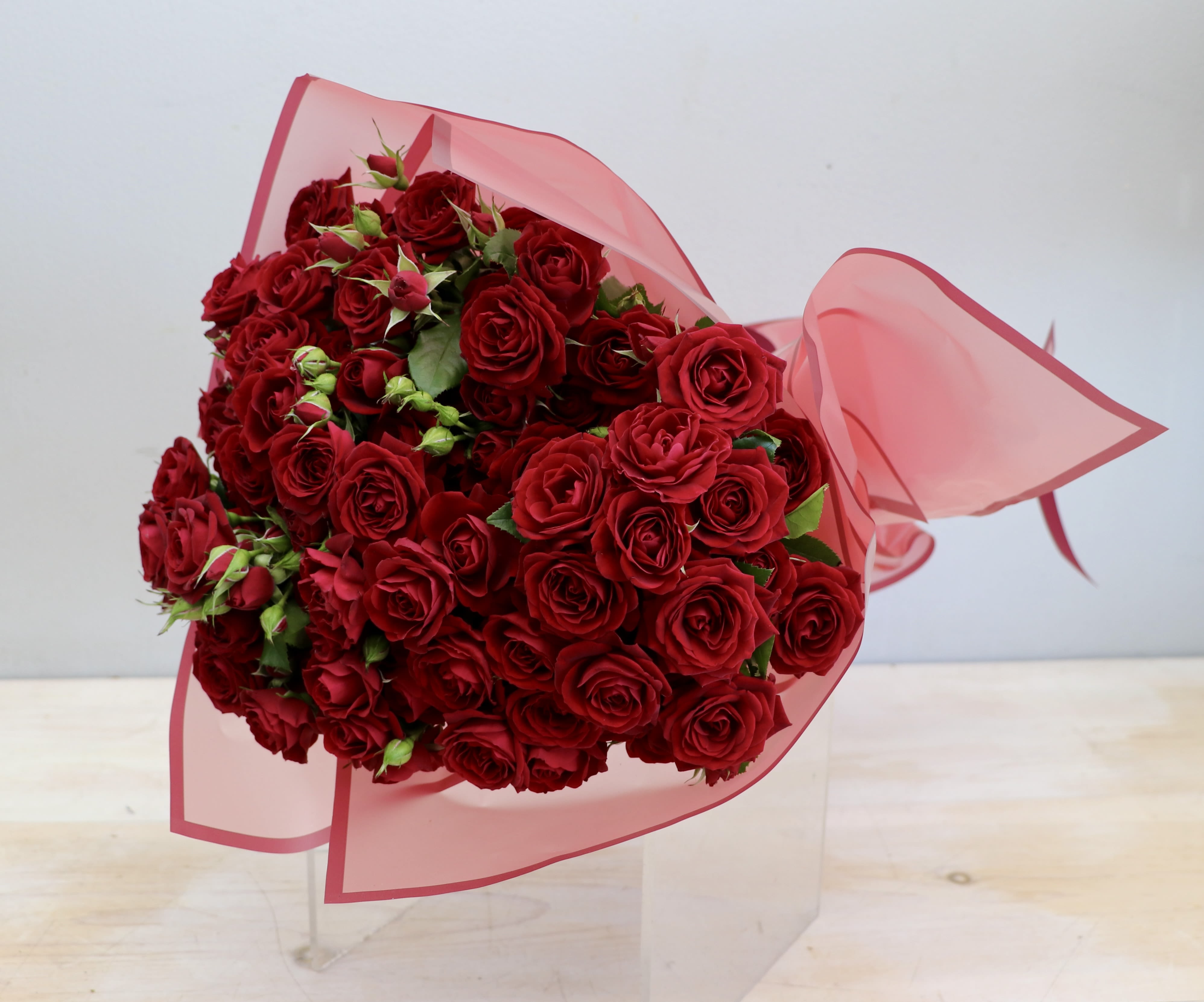 Large bouquet of red roses wrapped in pink translucent paper with a bow.