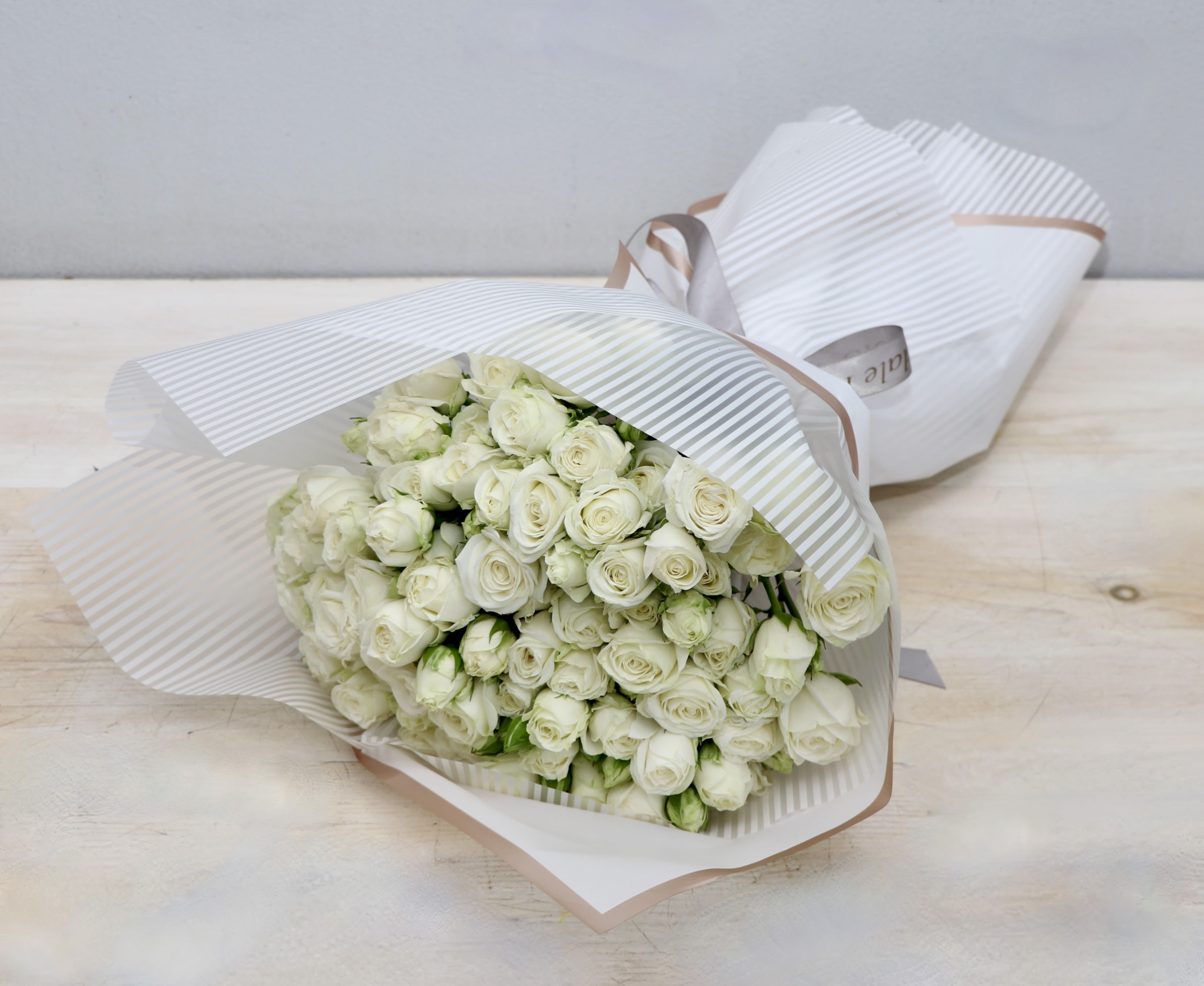 Large bouquet of white roses wrapped in striped white paper with a ribbon.