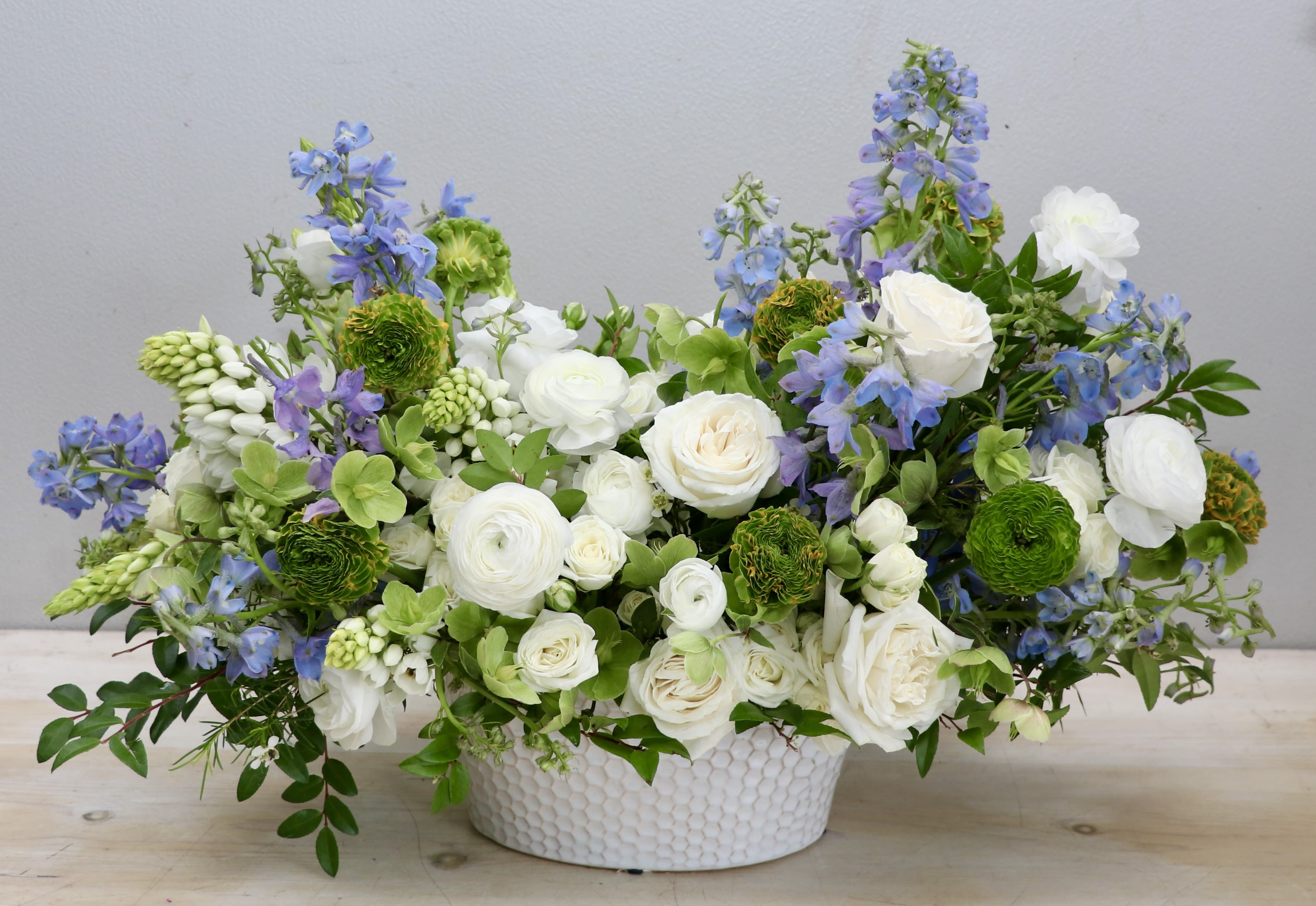 Low arrangement of white roses and ranunculus with blue flowers in a white ceramic bowl