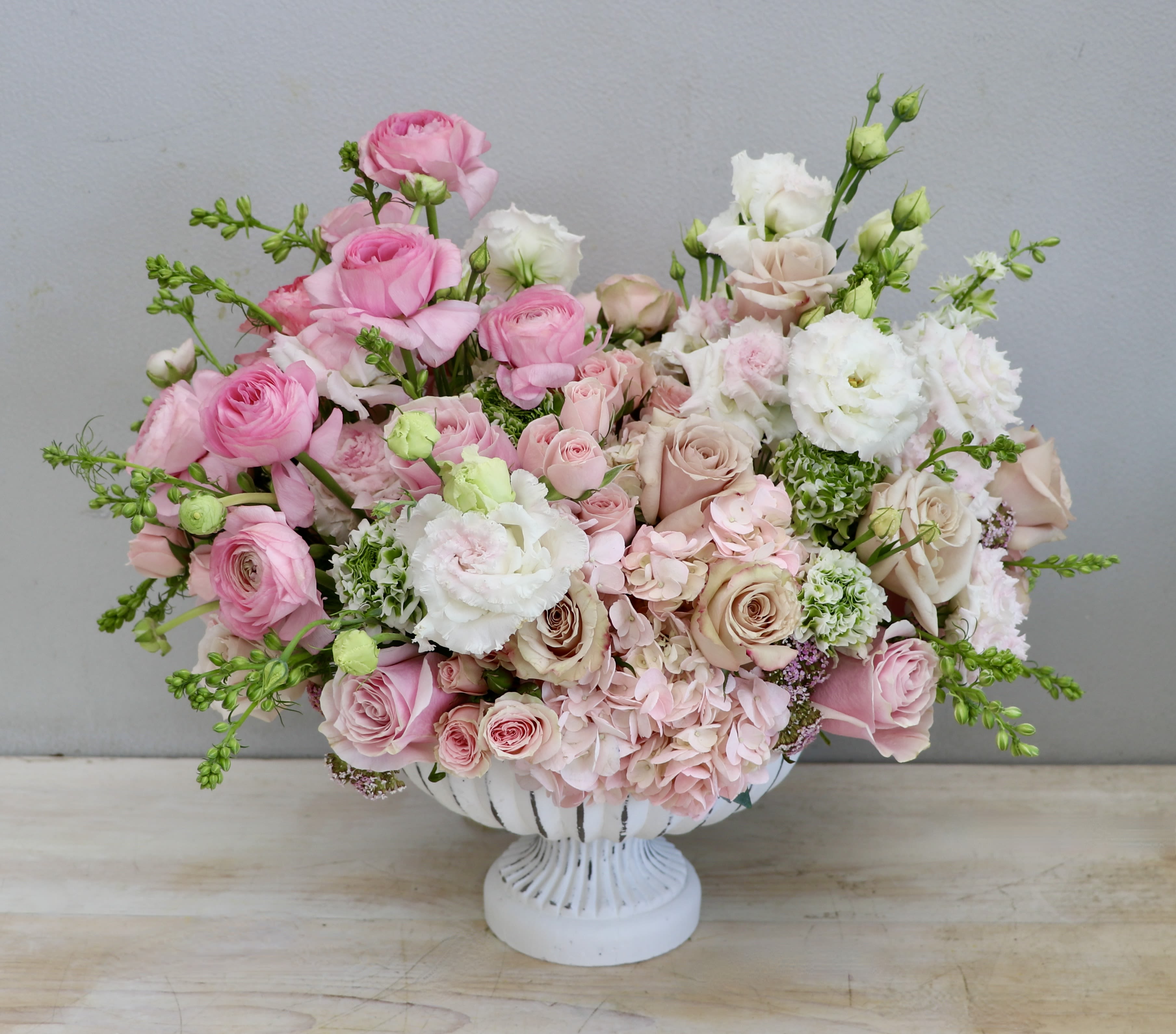 Low compote arrangement of pink and blush roses, hydrangeas, and white lisianthus in a white pedestal bowl
