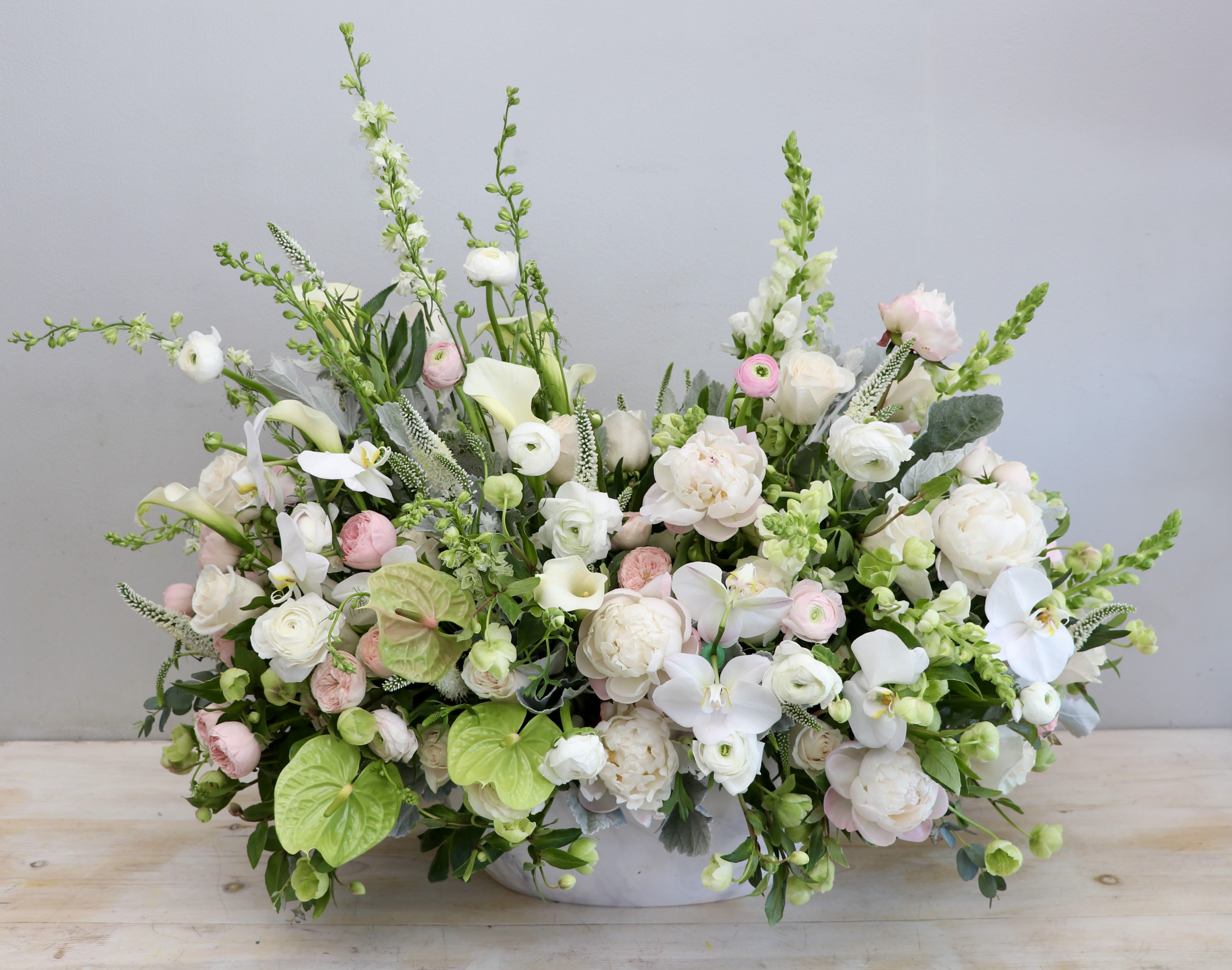Low, wide arrangement of white and blush flowers with orchids and calla lilies in a white bowl