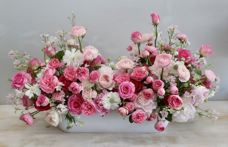 Low centerpiece of pink and white roses and ranunculus in a long white container
