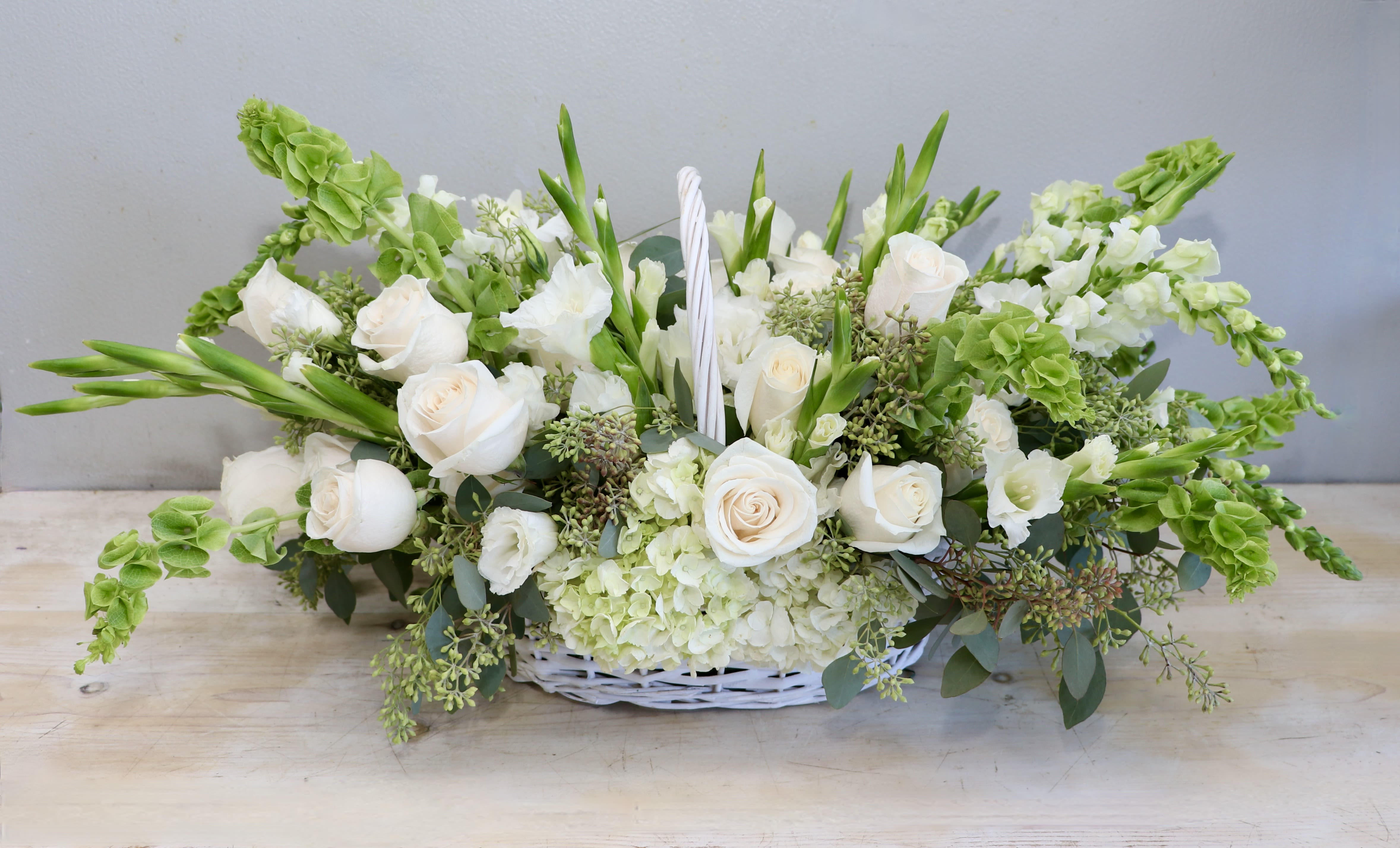 Low white and green floral basket with white roses, hydrangeas, and bells of Ireland